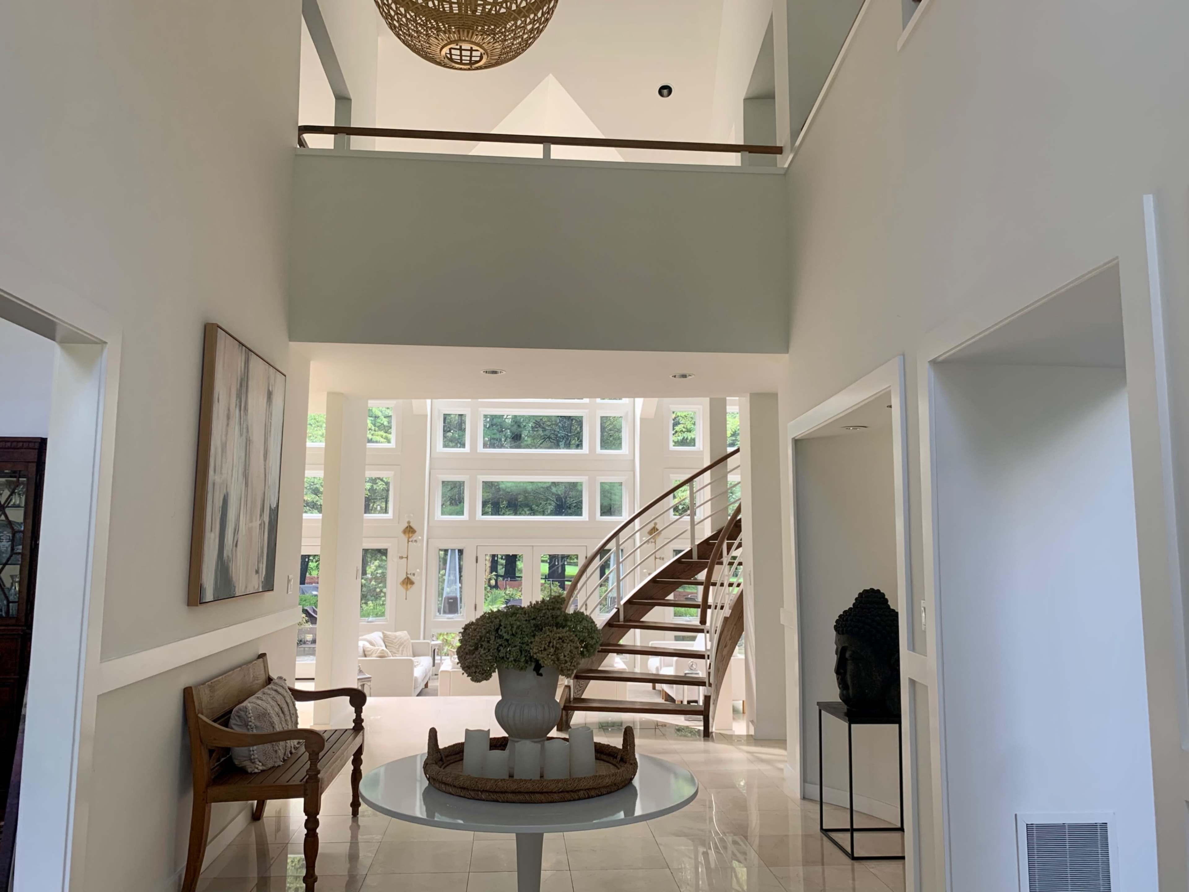 A spacious entryway with a circular table, a wooden staircase, and large windows allowing natural light to illuminate the interior.
