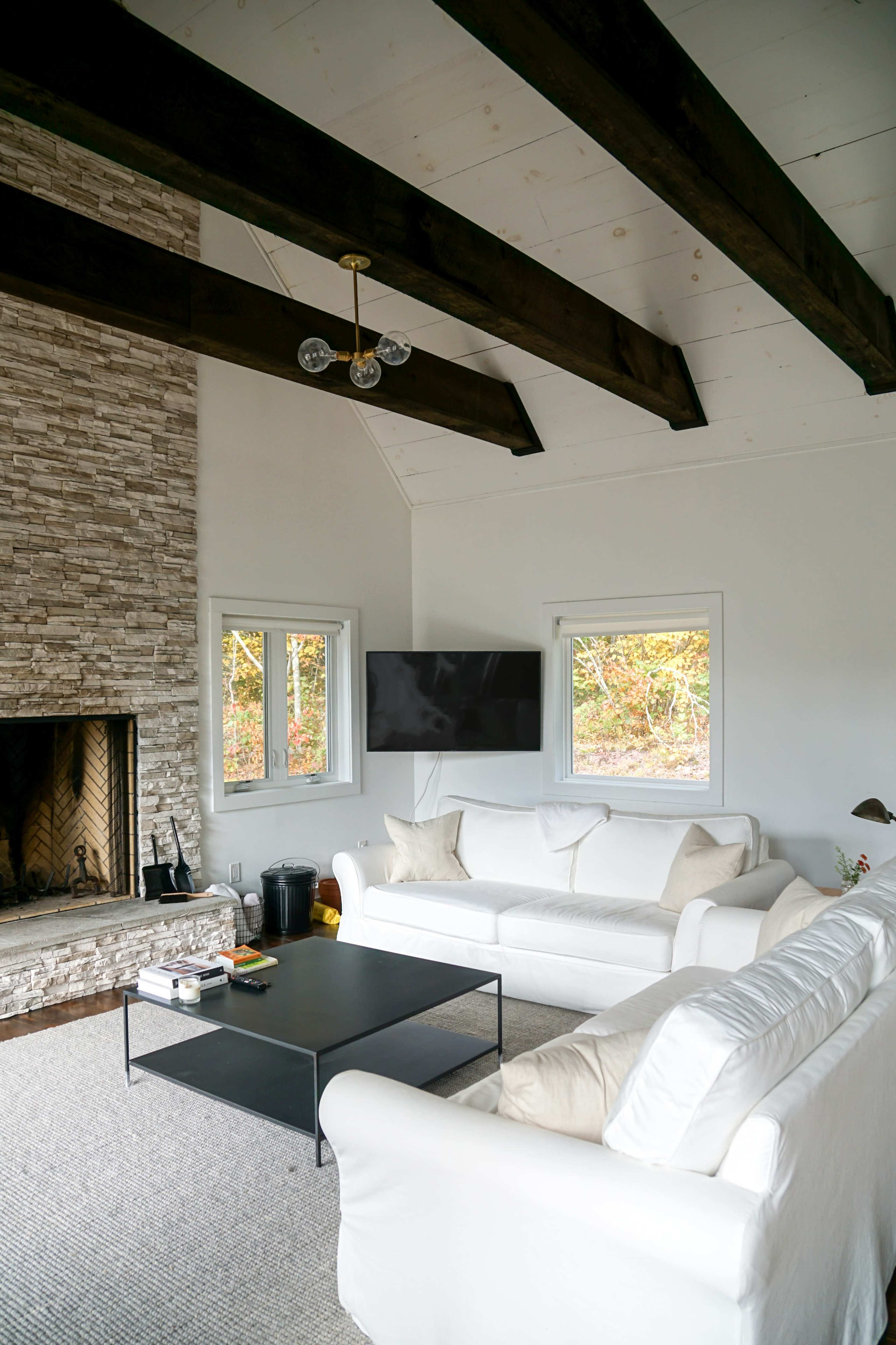 The living room features a stone fireplace, white sofas, a black coffee table, and large windows that offer natural light.