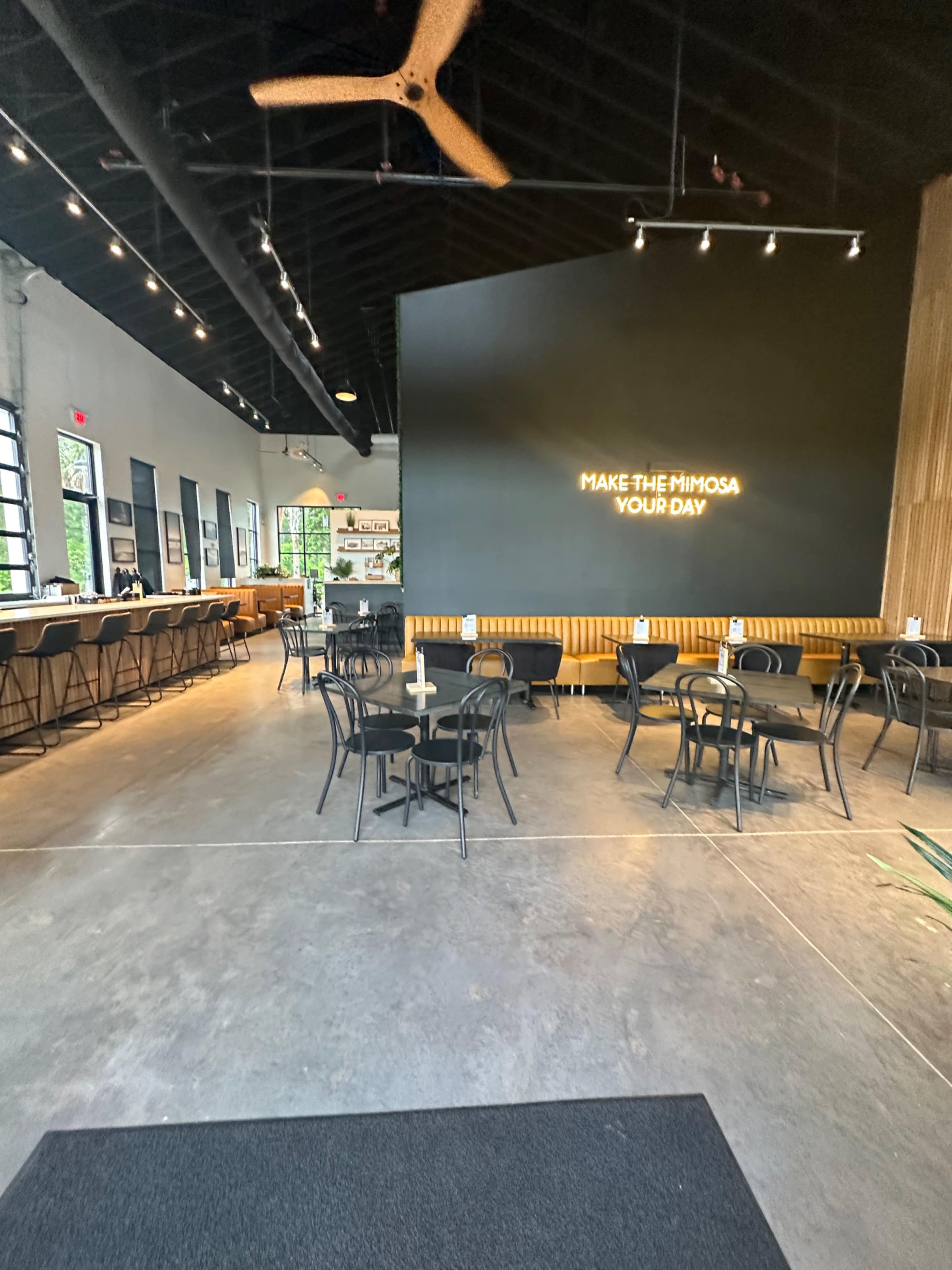 The image shows a modern restaurant interior with a black accent wall, seating arranged around tables, and a bar area in the background.