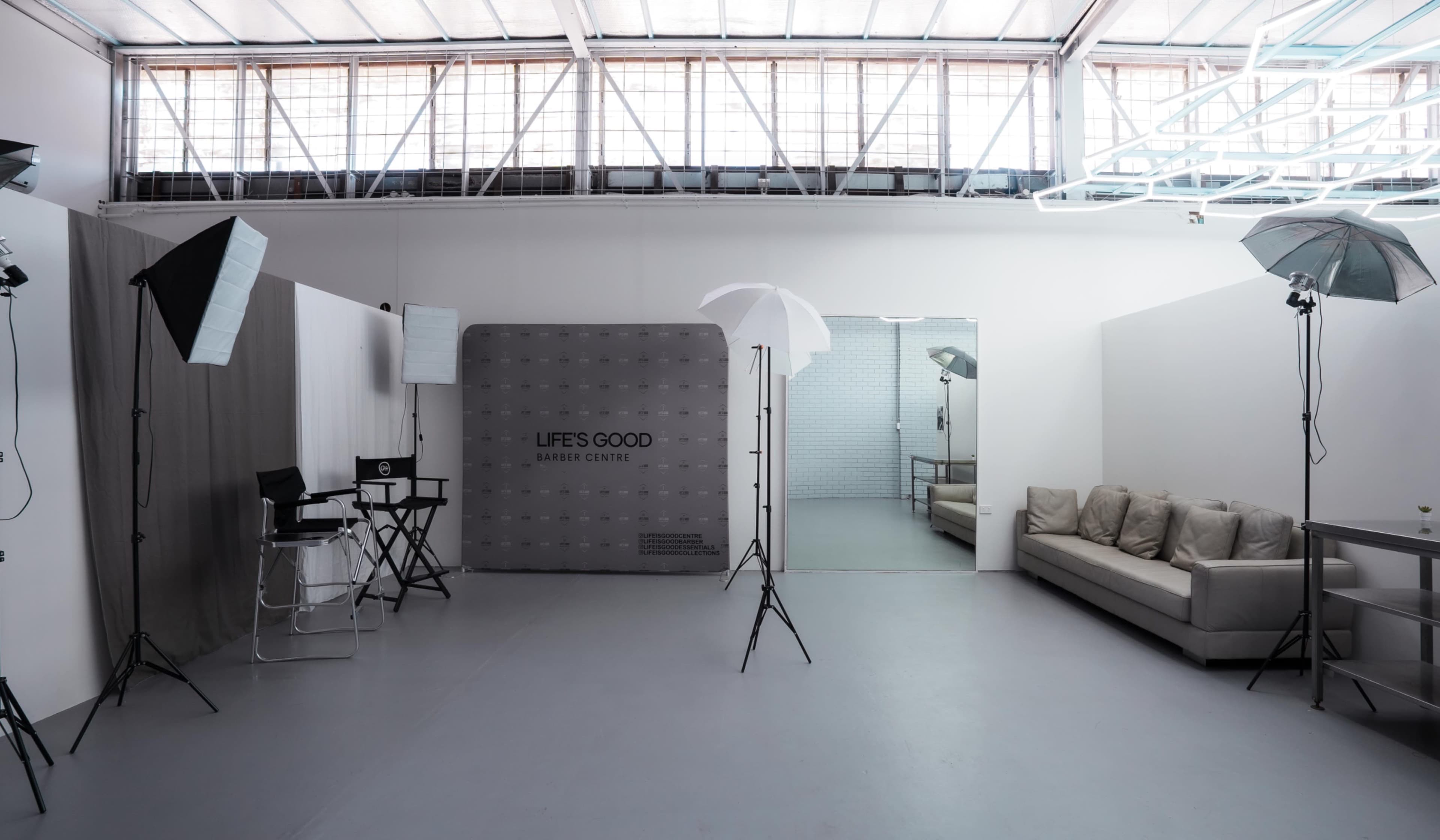 The image shows a spacious photography studio with soft lighting equipment, a large mirror, and a beige sofa along one wall.