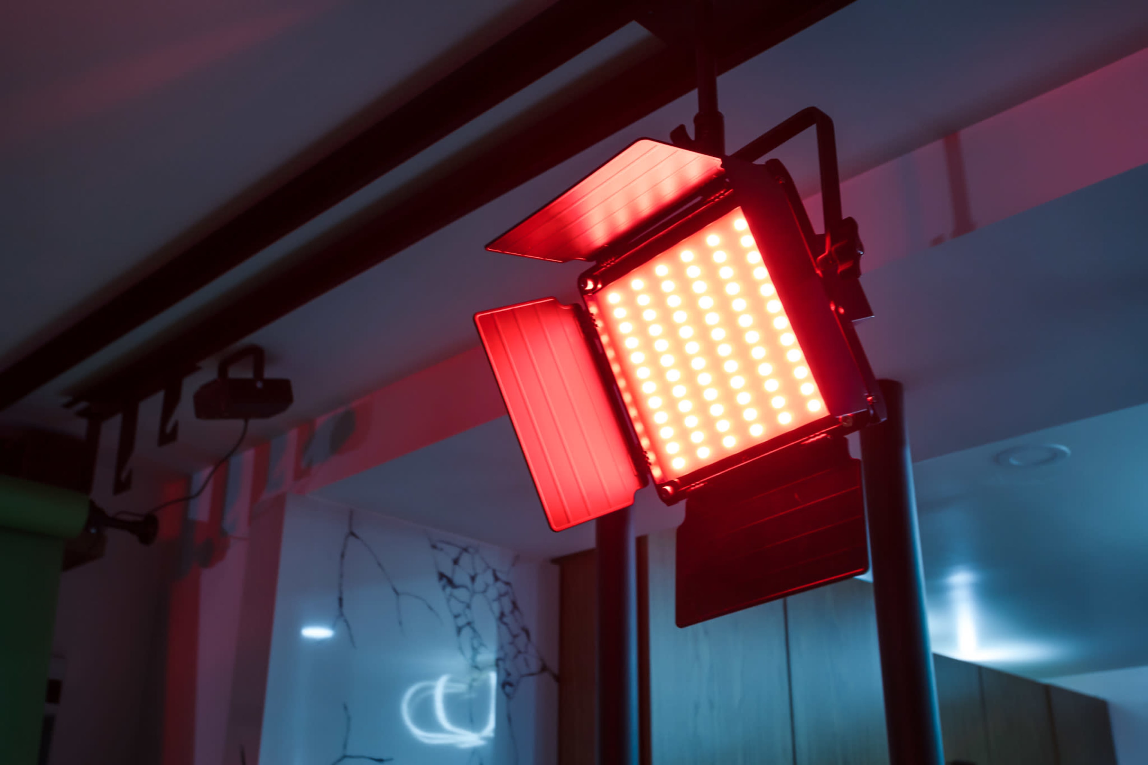 A red LED light panel is mounted on a stand with barn doors partially open.