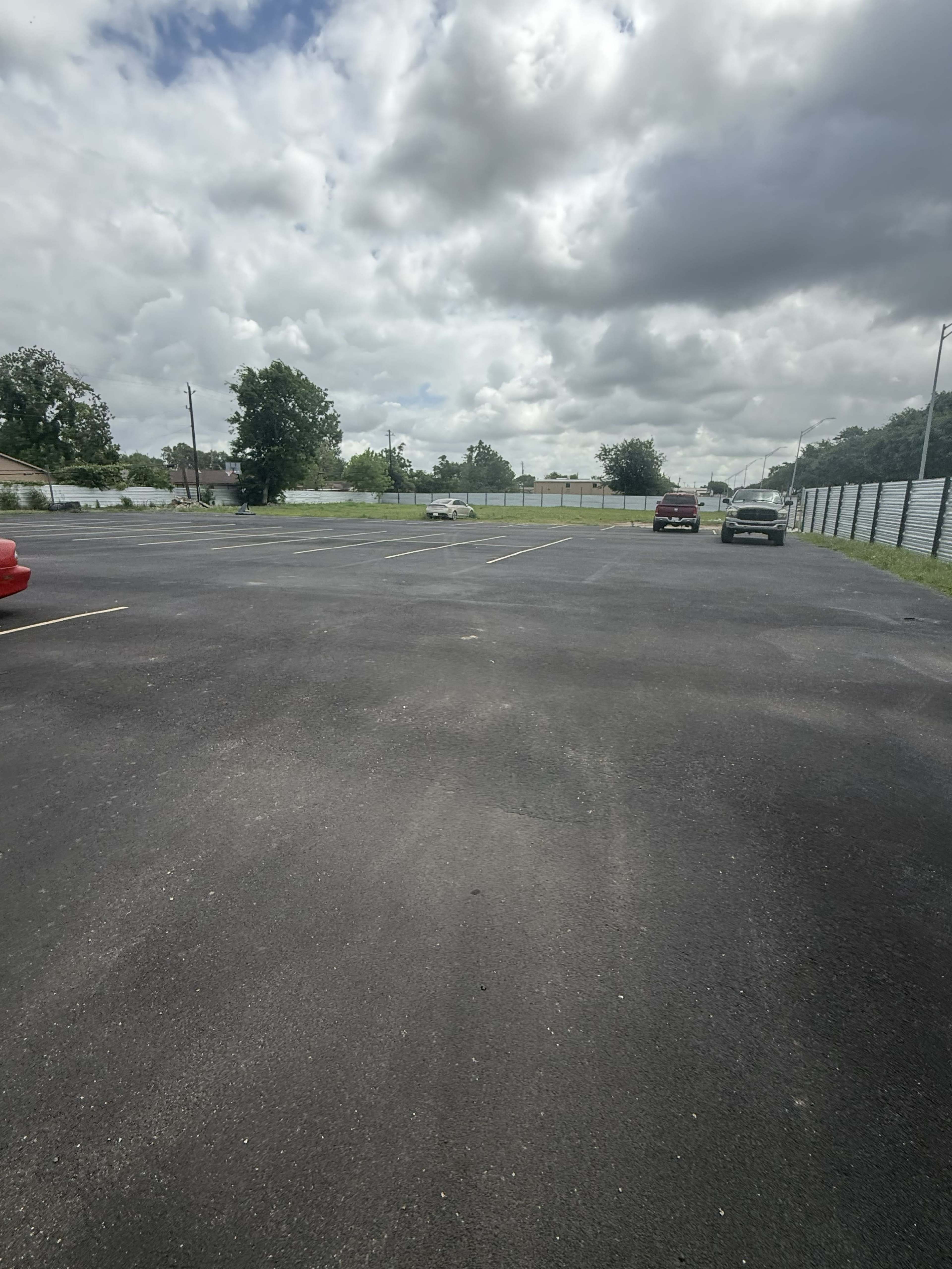 The image shows an empty parking lot with a few parked vehicles under a cloudy sky.