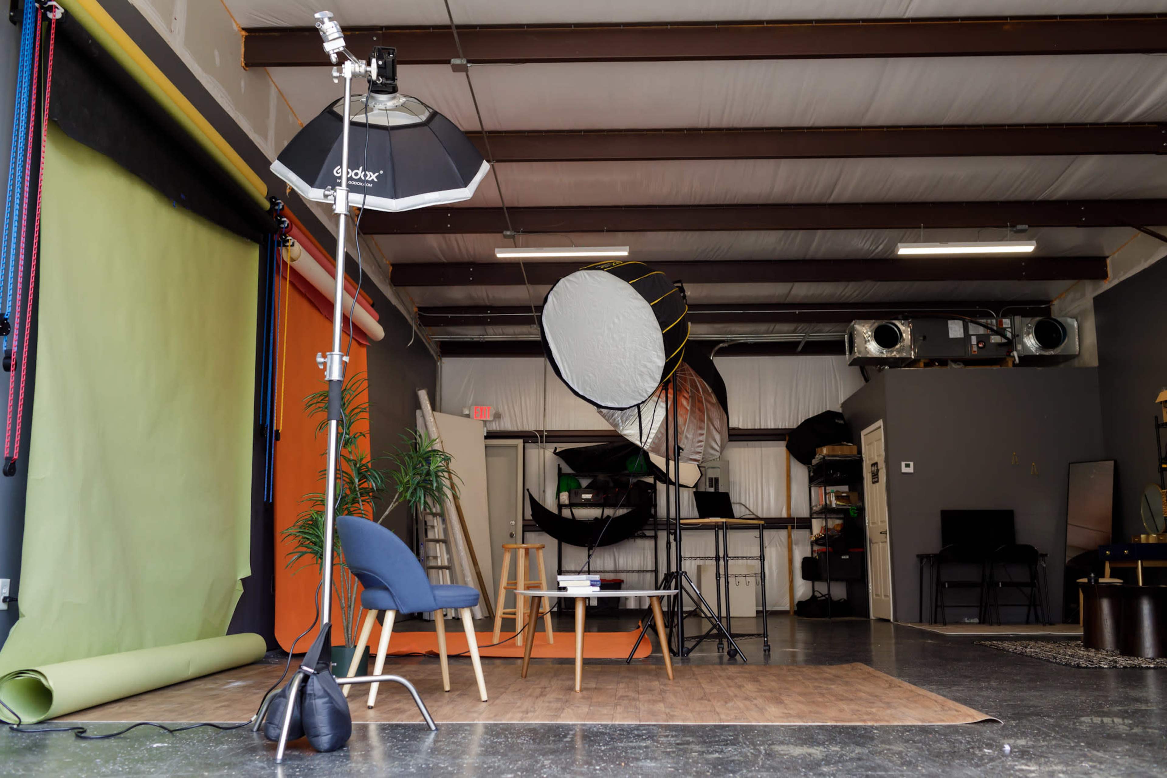 A photography studio equipped with backdrop stands, lighting equipment, and a seating area.