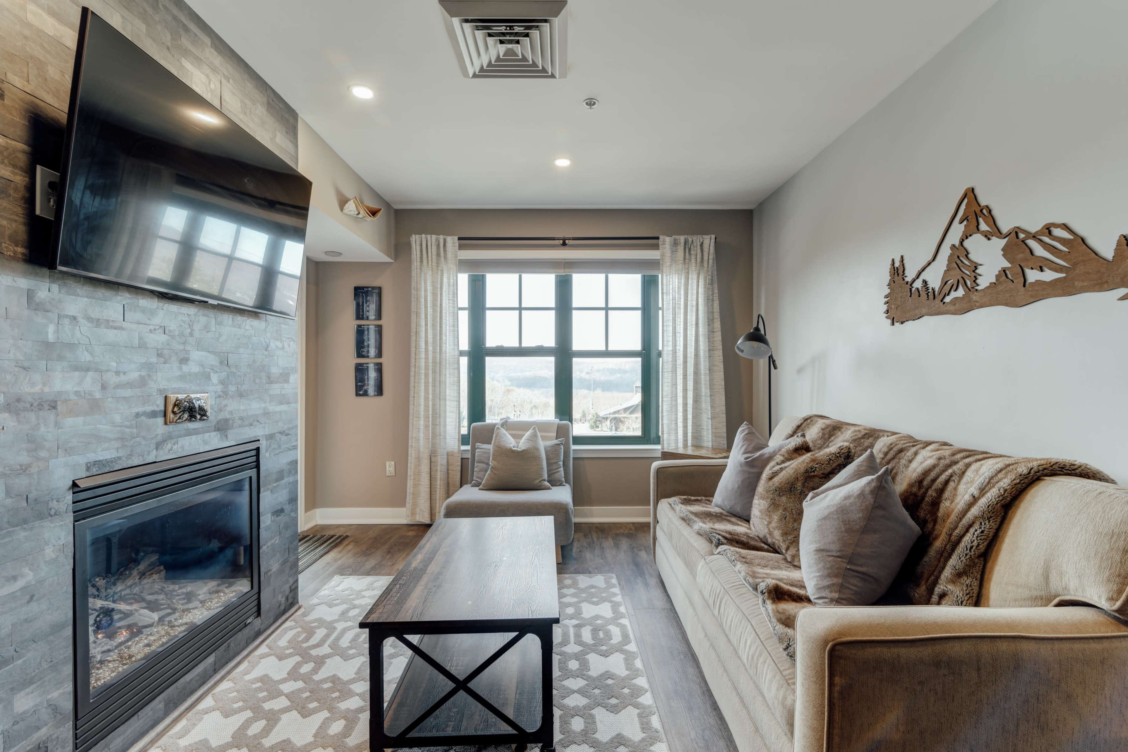 A living room with a fireplace, a sofa, a coffee table, and a large window overlooking a mountain view.