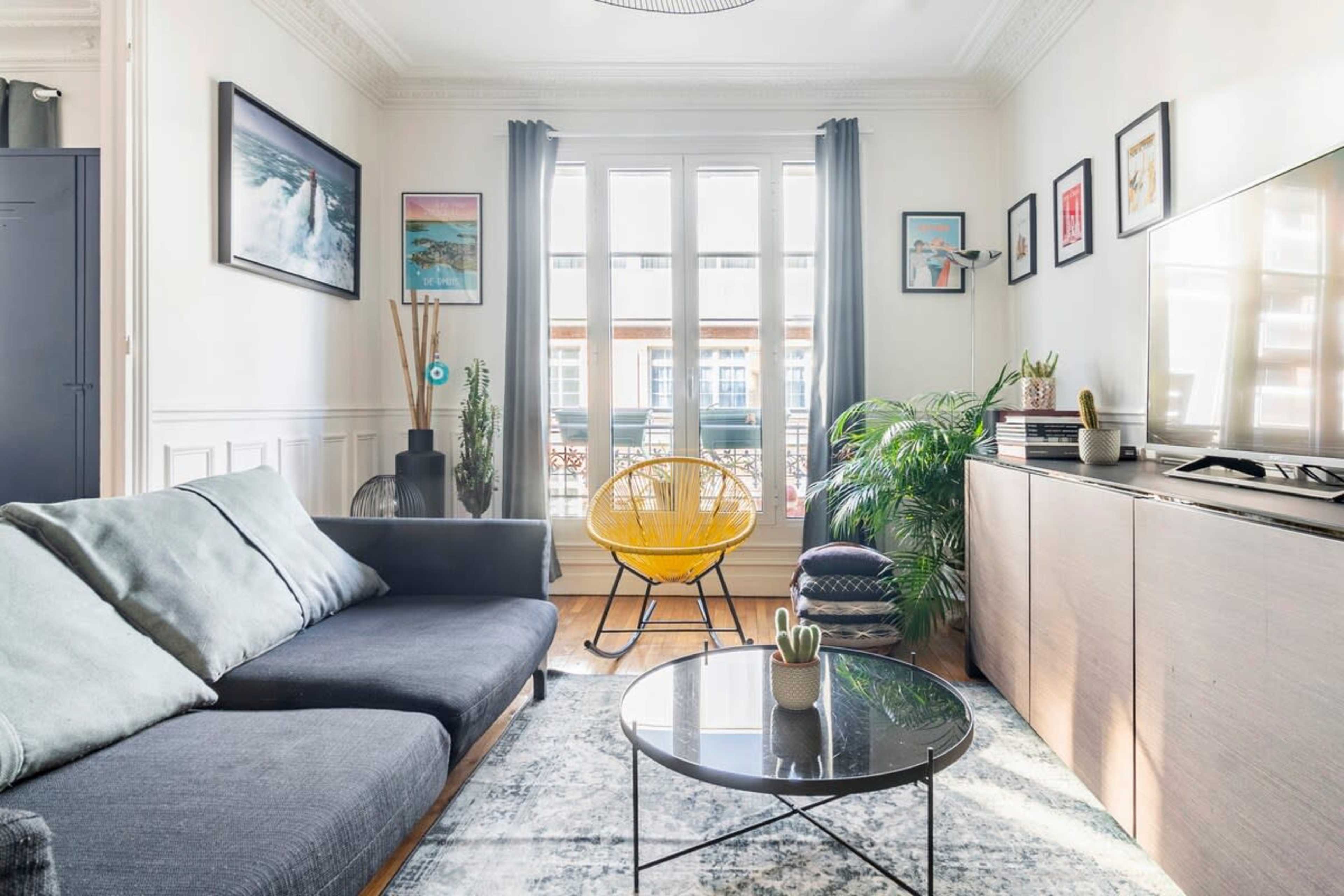 A modern living room with a dark sofa, a round coffee table, and a bright yellow accent chair, illuminated by natural light from large windows.