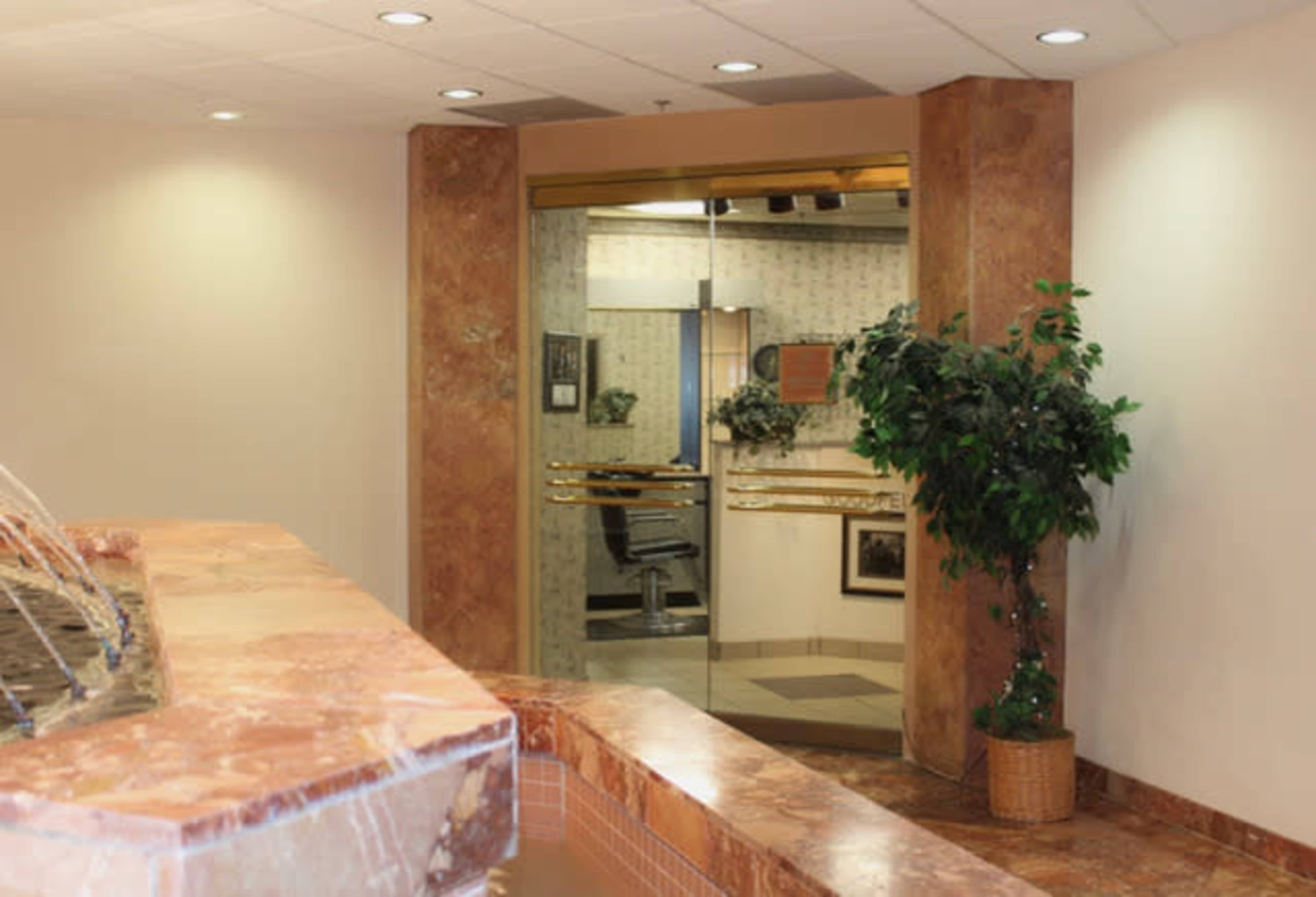 The image shows a modern lobby area with a water fountain, potted plant, and glass doors leading to an office space.
