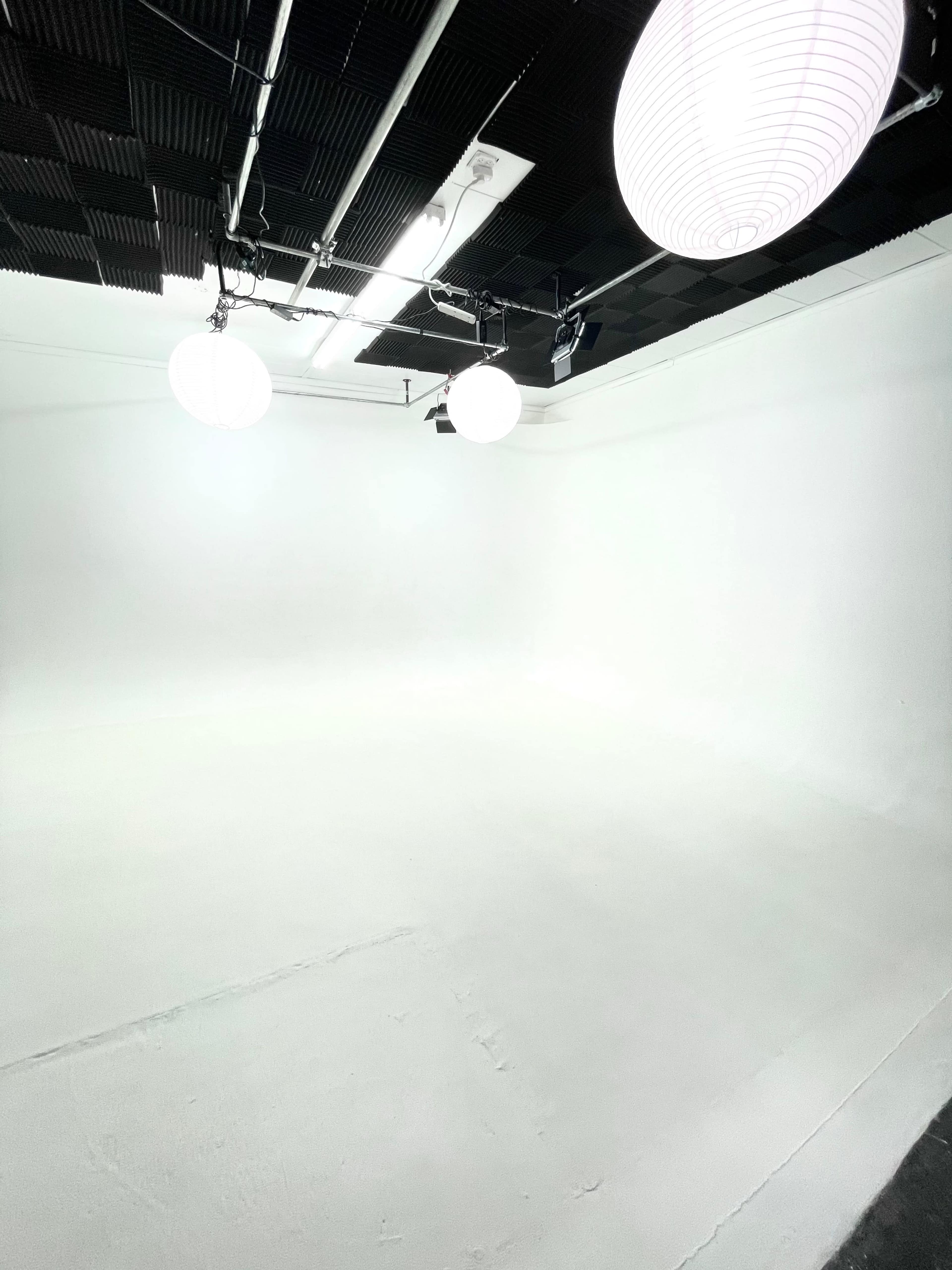 A minimalist white studio space with three round hanging lights and a smooth floor.