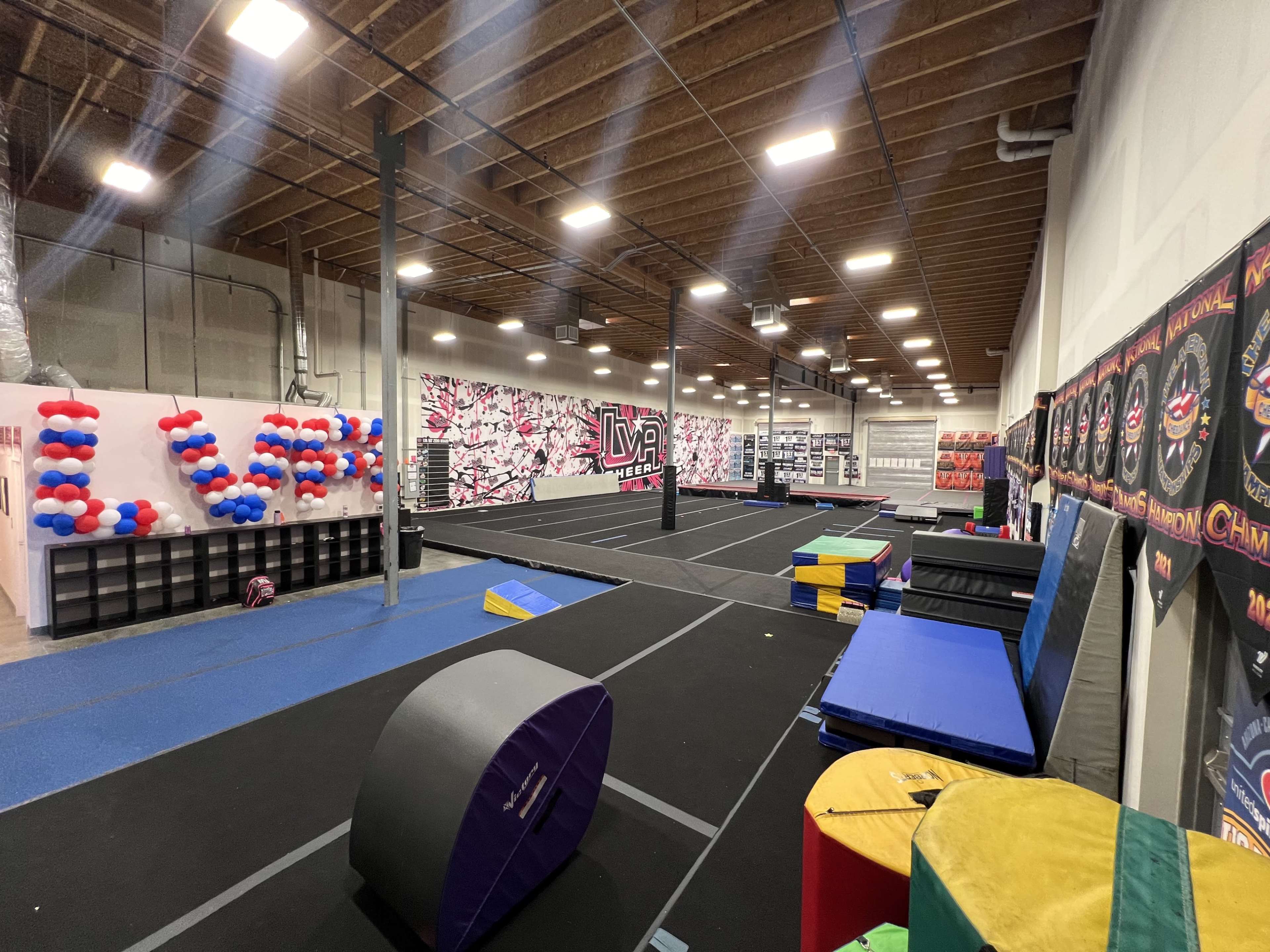 A spacious gymnasium equipped with various gymnastic apparatus, colorful mats, and walls decorated with murals.