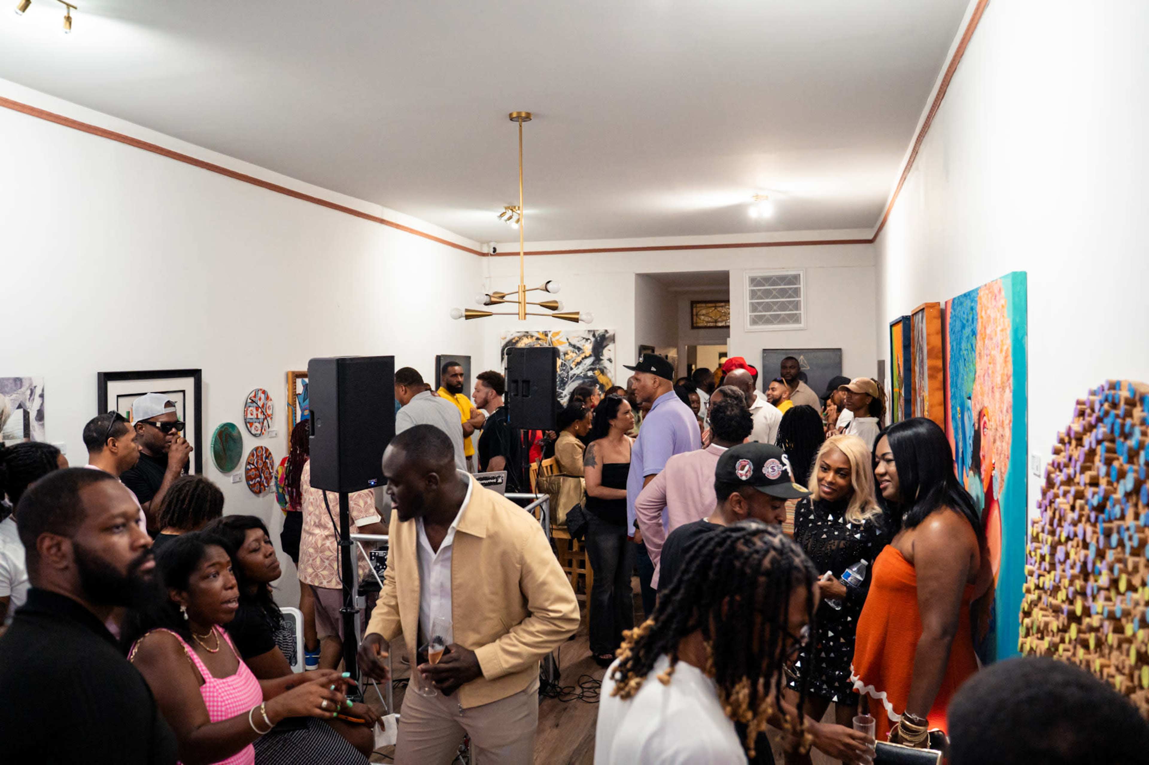A diverse crowd of people gathers in an art gallery, engaging in conversation while surrounded by colorful artworks on the walls.