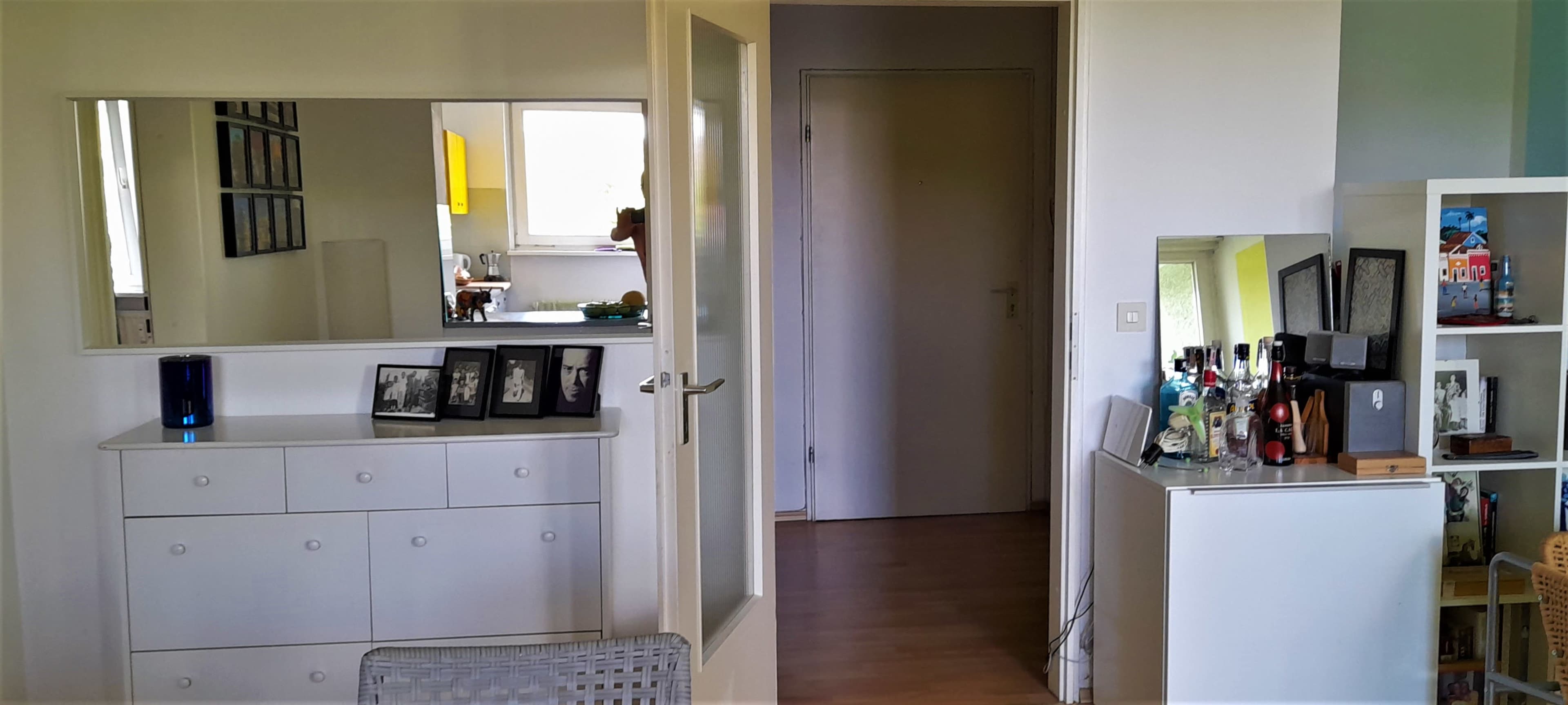 The image shows an interior space featuring a mirrored dresser with framed photographs and a bar station beside a door leading to another room.