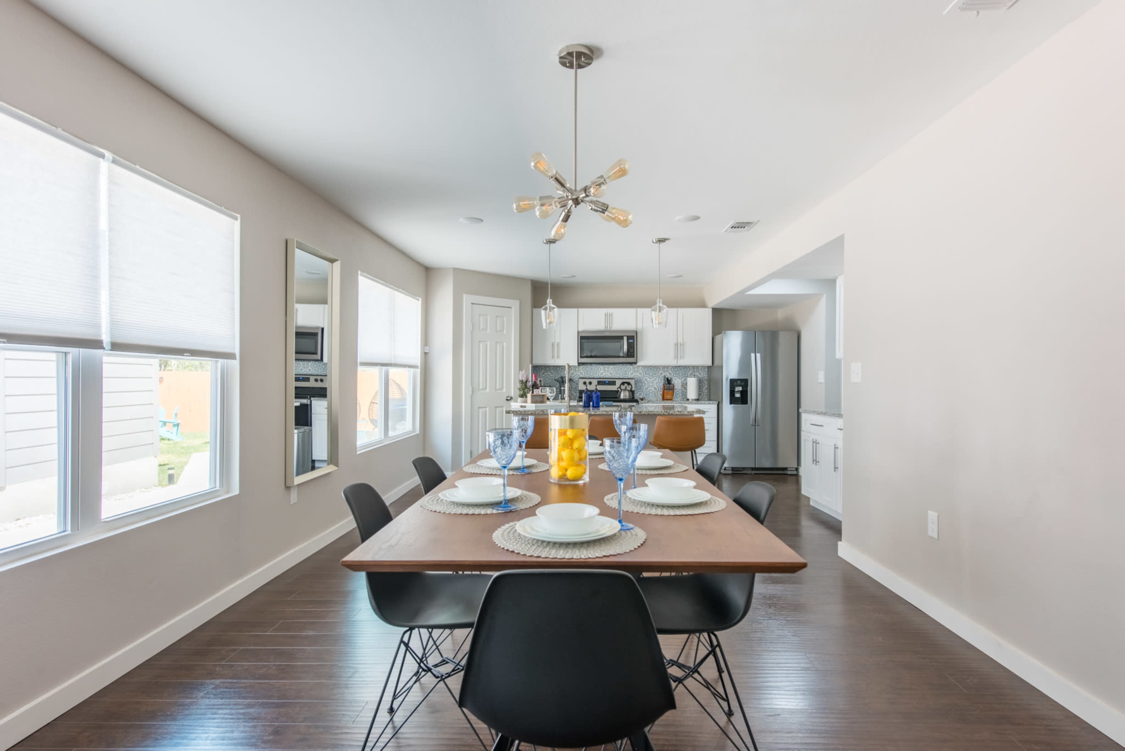 A dining area with a wooden table set for four, featuring a modern light fixture, and leading into a kitchen space in an open-concept layout.