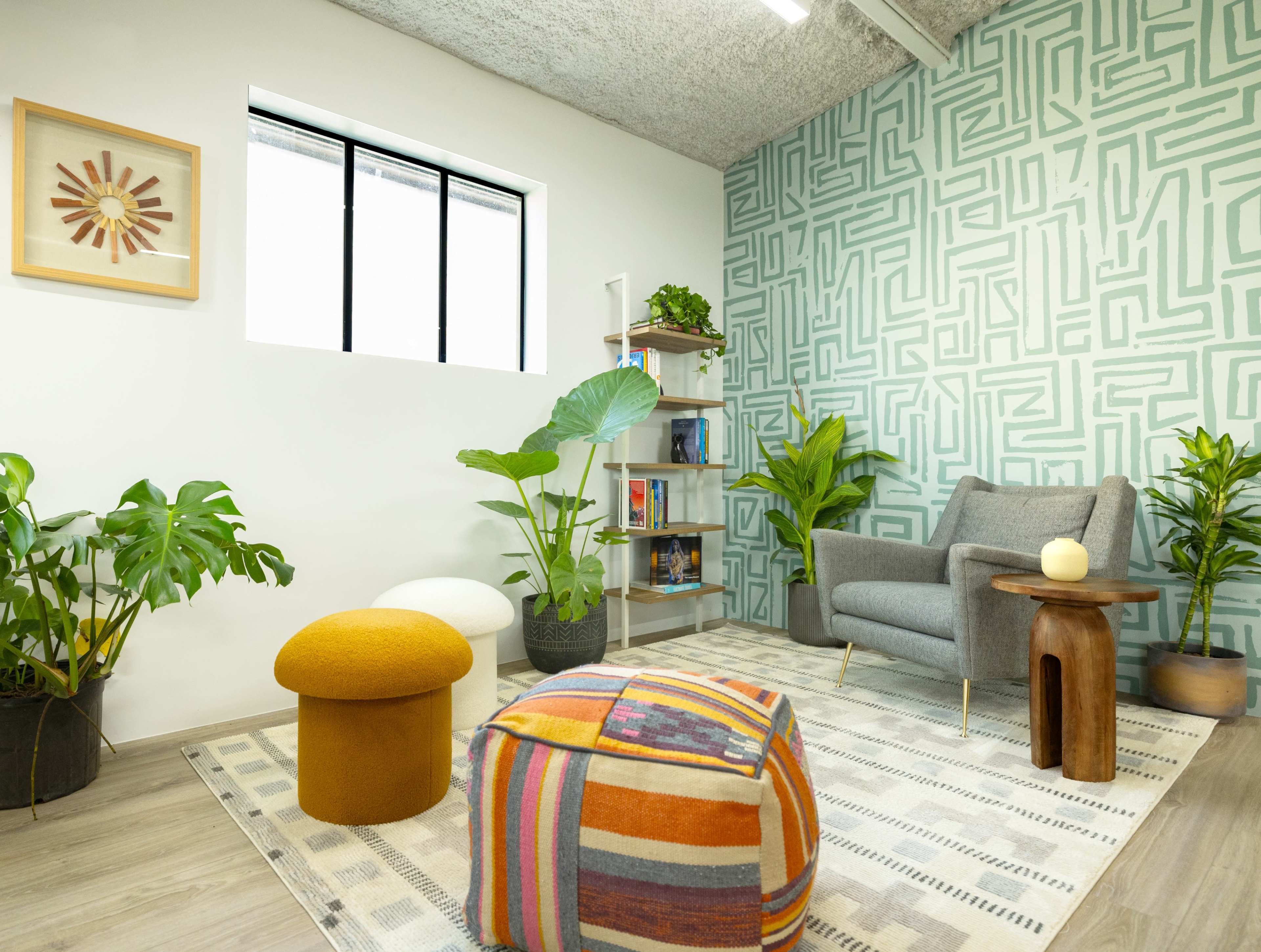 A modern, inviting room with a patterned accent wall, a gray armchair, potted plants, and colorful decorative elements.