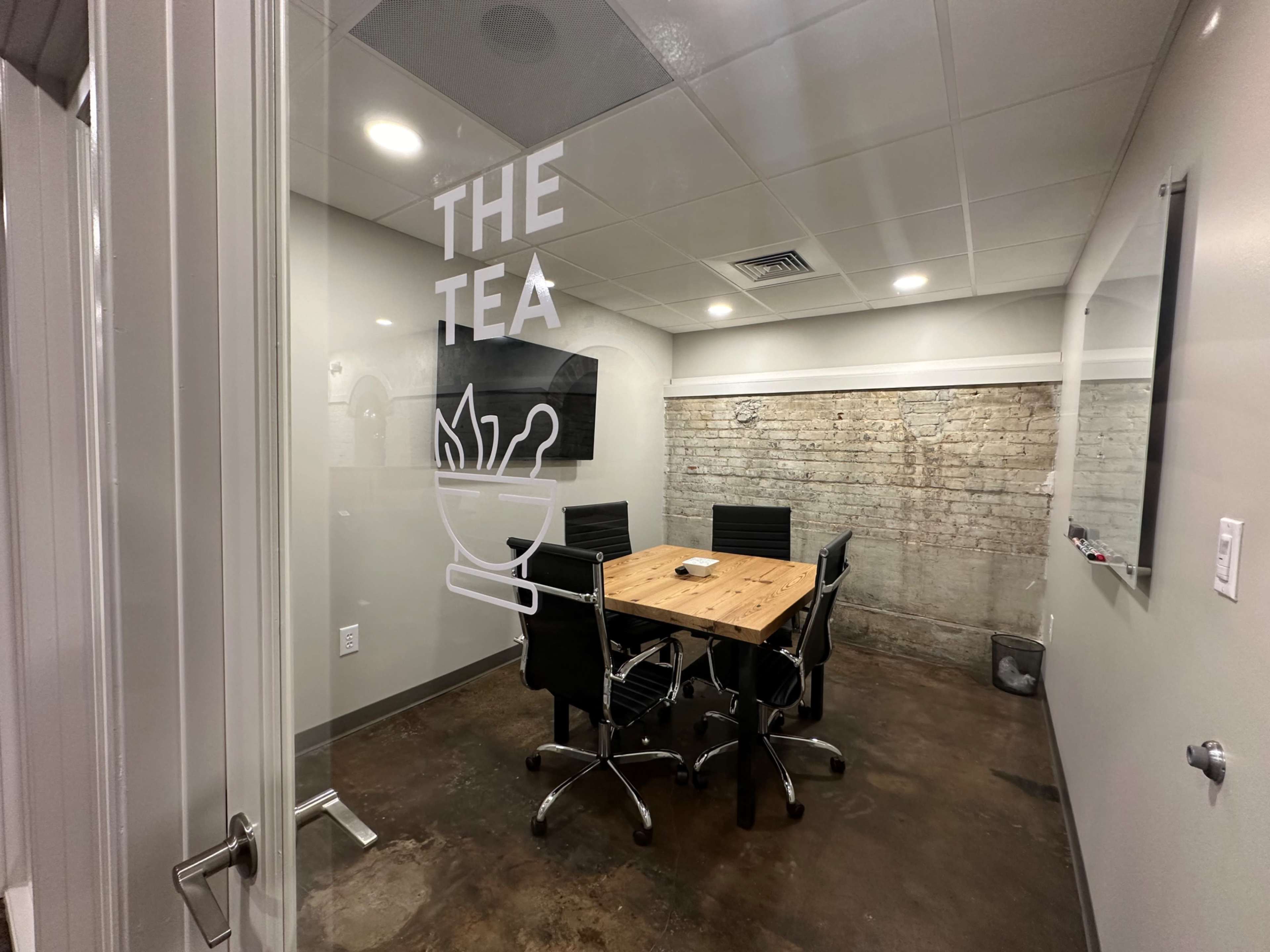 A conference room with a wooden table and black chairs is visible through a glass door labeled "THE TEA."