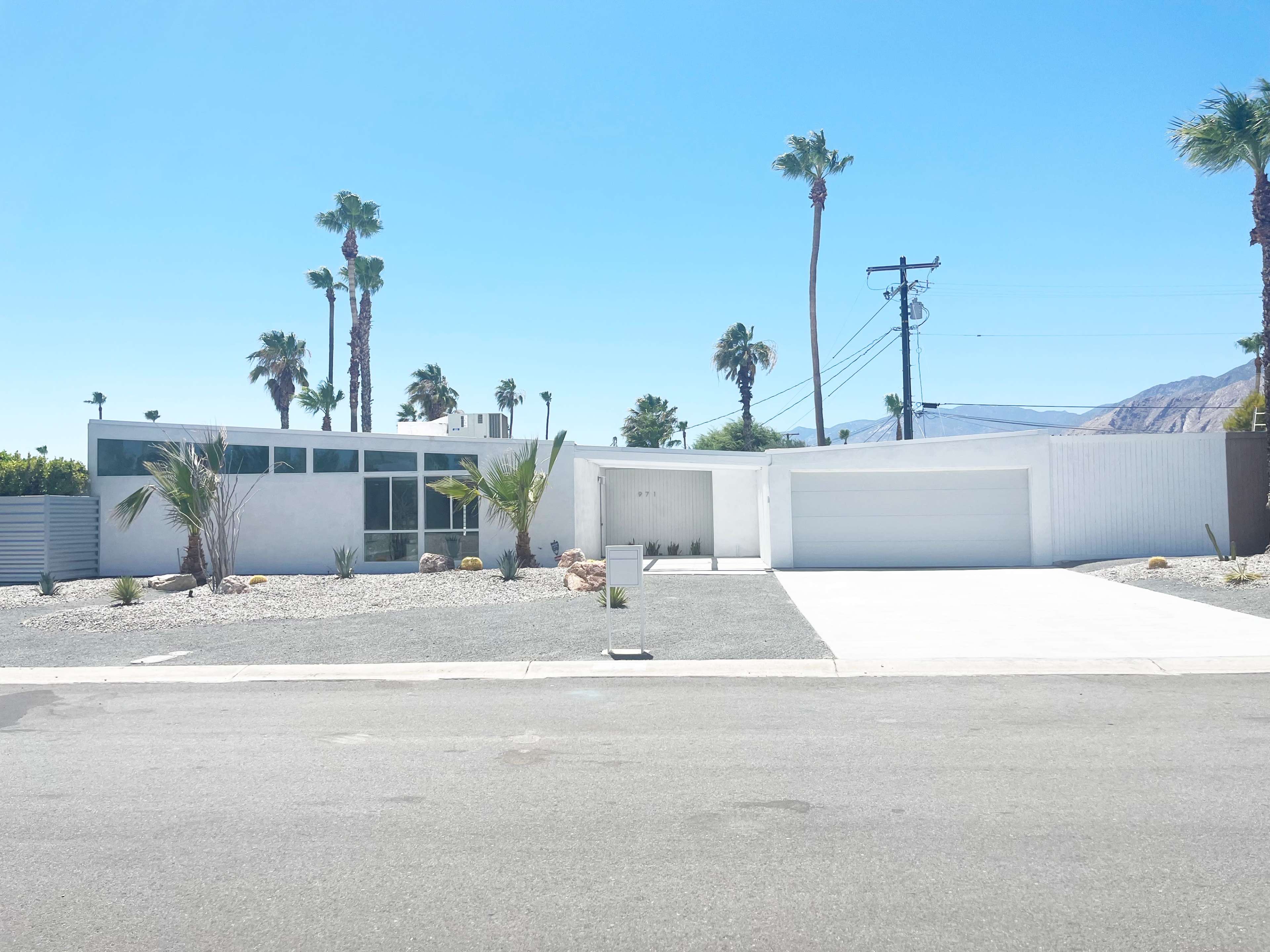 A modern single-story house with a gravel front yard and palm trees is located on a quiet street.