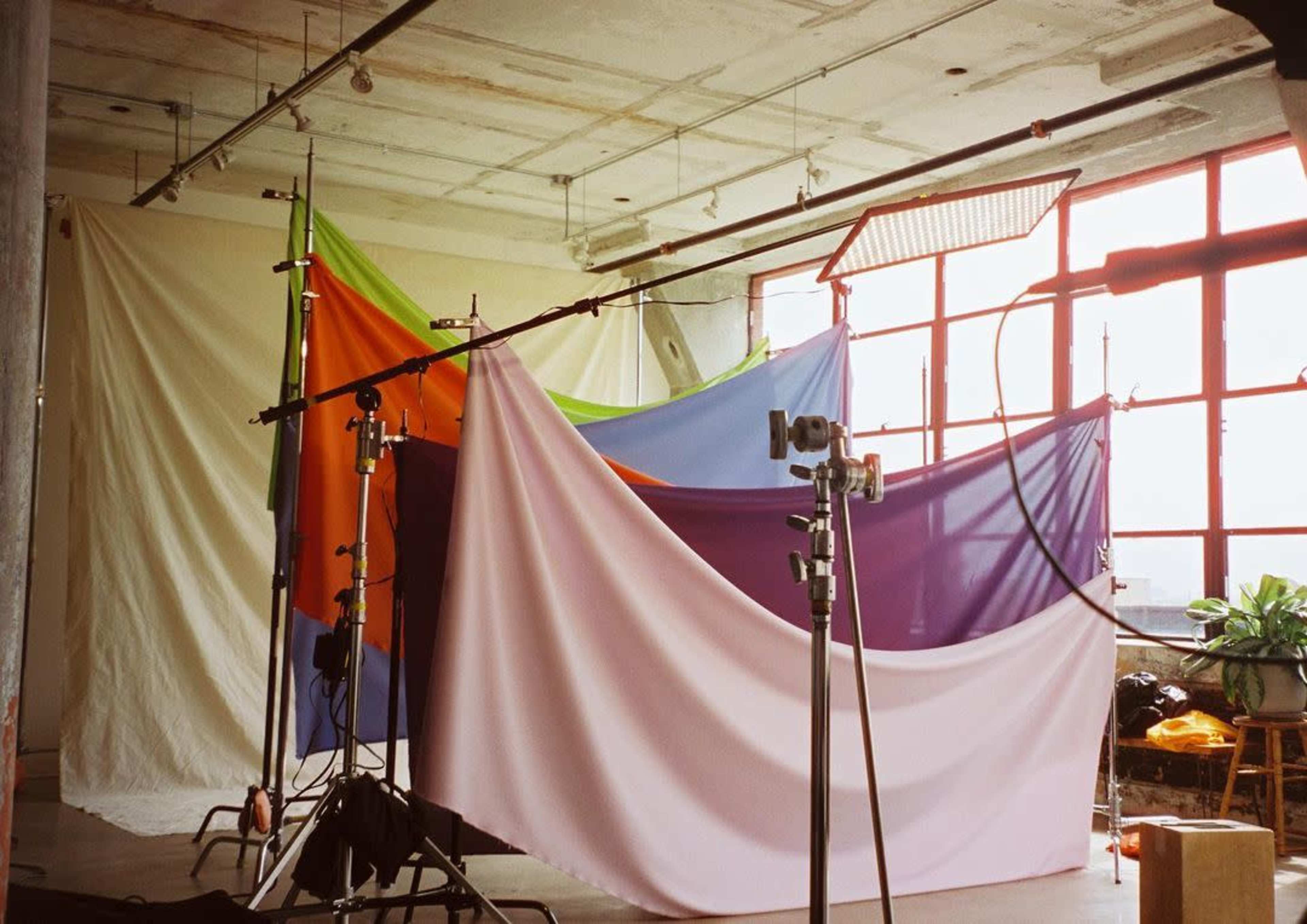 A photography studio with colorful backdrops draped over stands and large windows allowing natural light to enter the space.