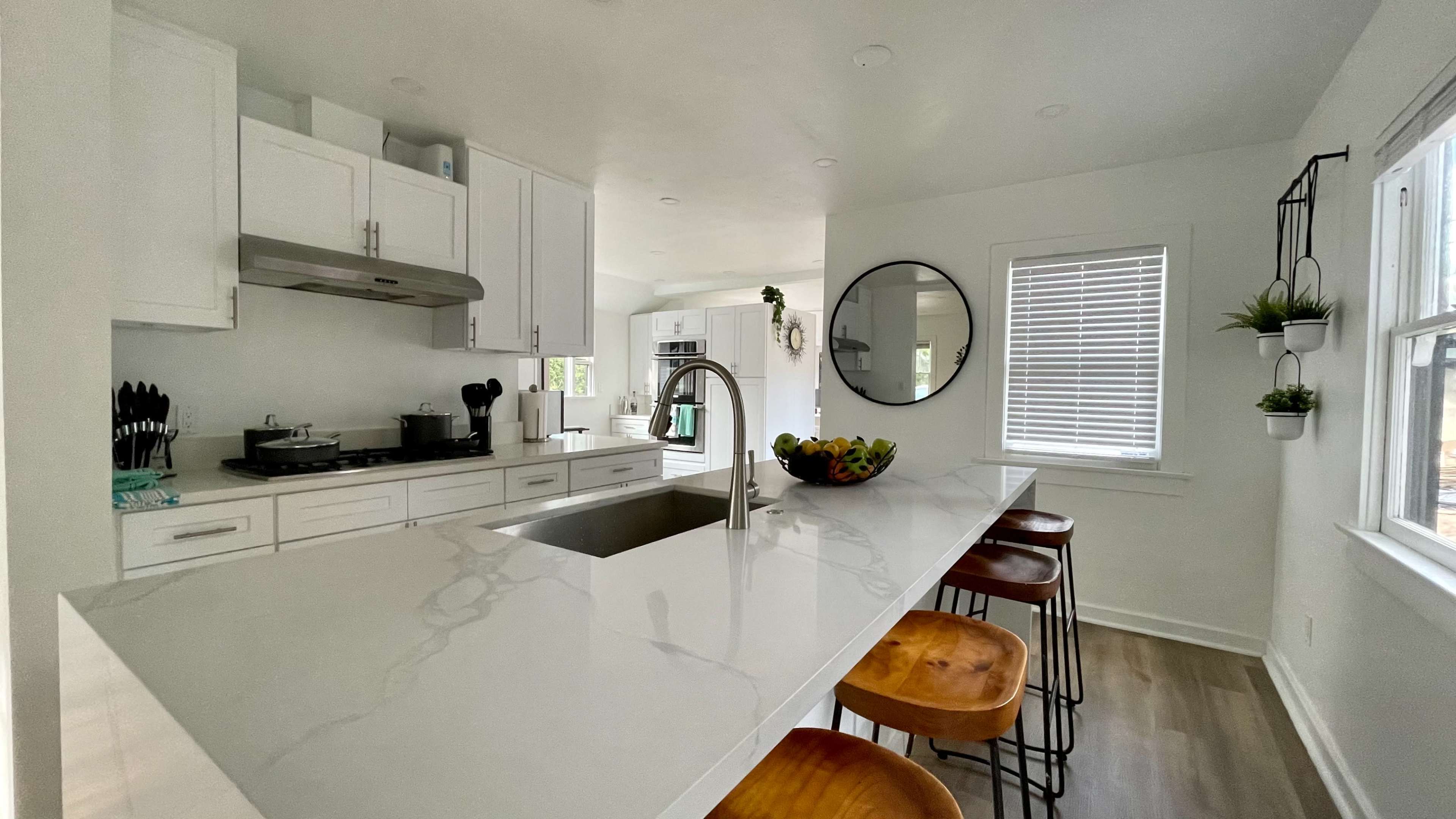 A modern kitchen features white cabinetry, a large island with a sink, and three wooden bar stools.
