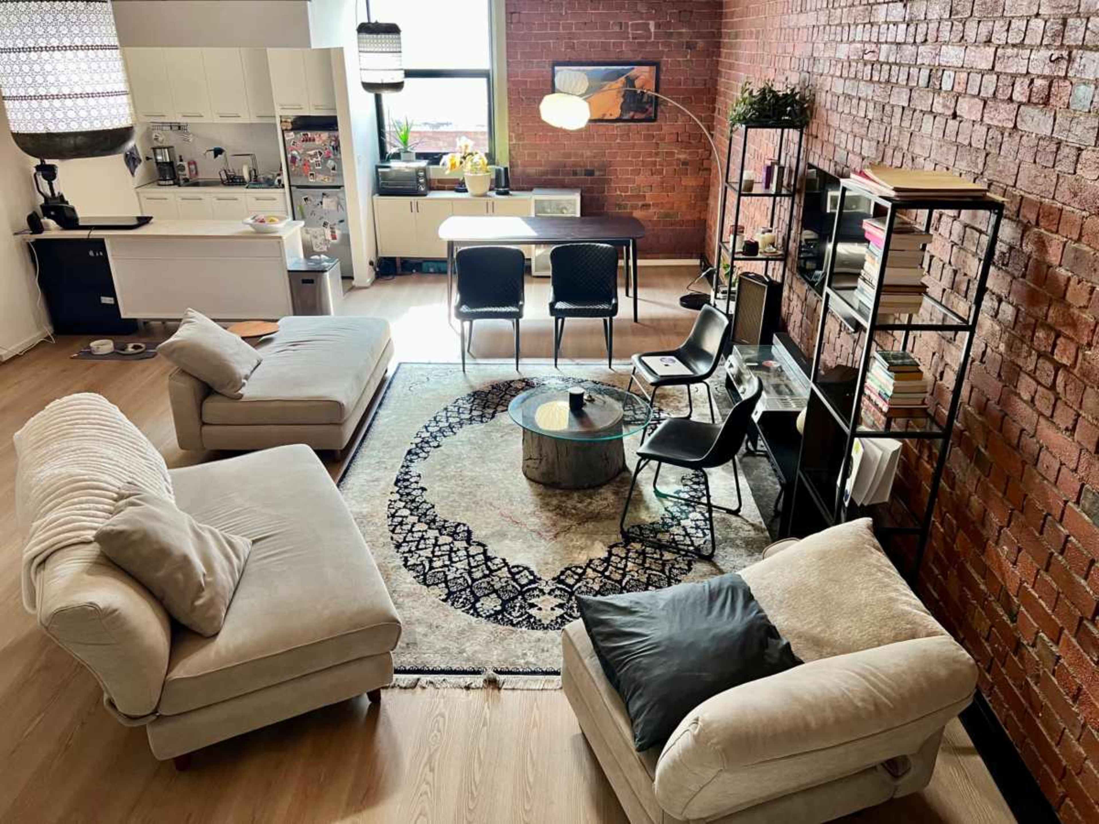 The image shows a modern living space with a kitchen area, a dining table with chairs, and a cozy seating arrangement on a patterned rug.