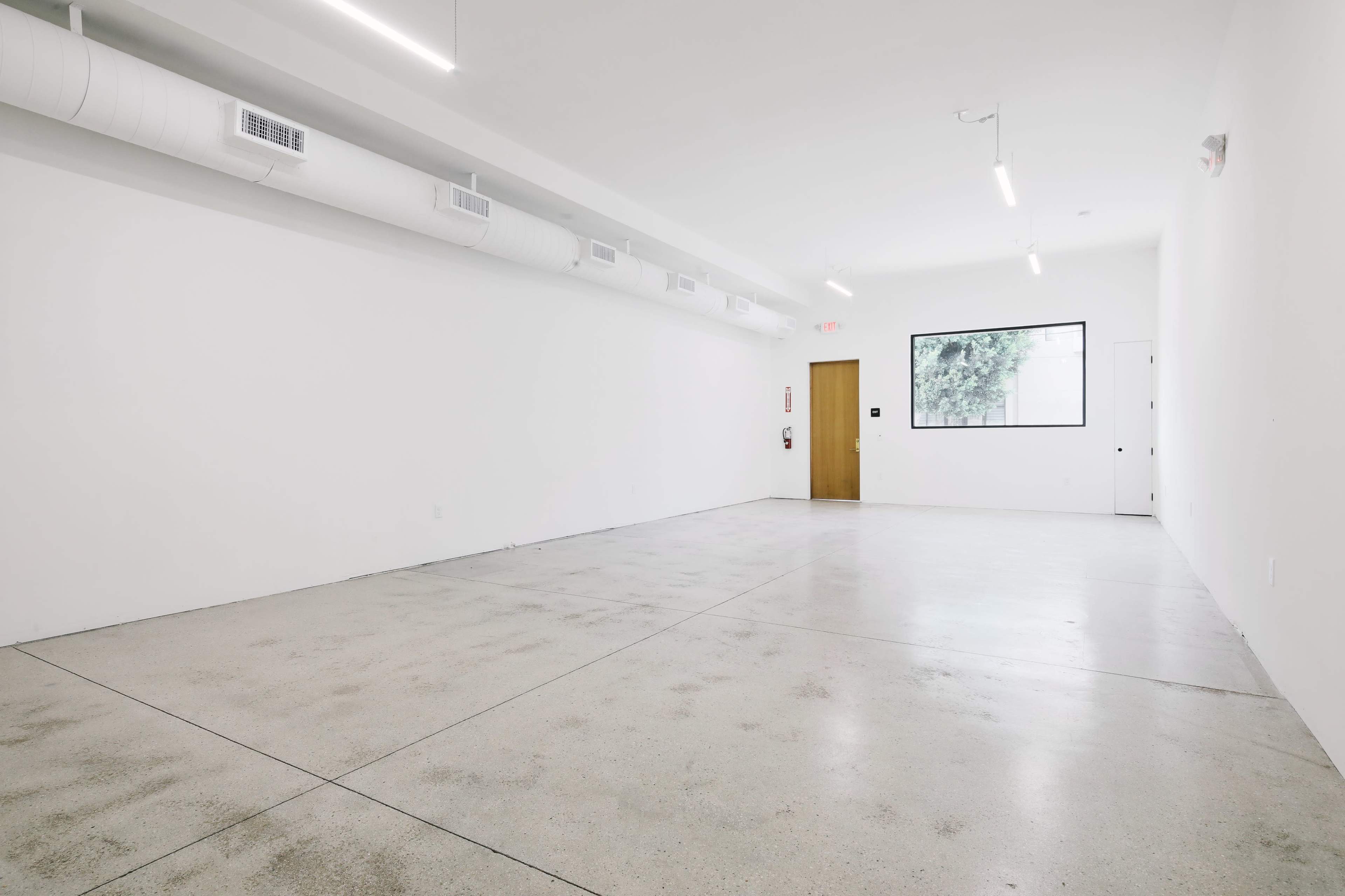 An empty room with a polished concrete floor, white walls, and a window on the far side.