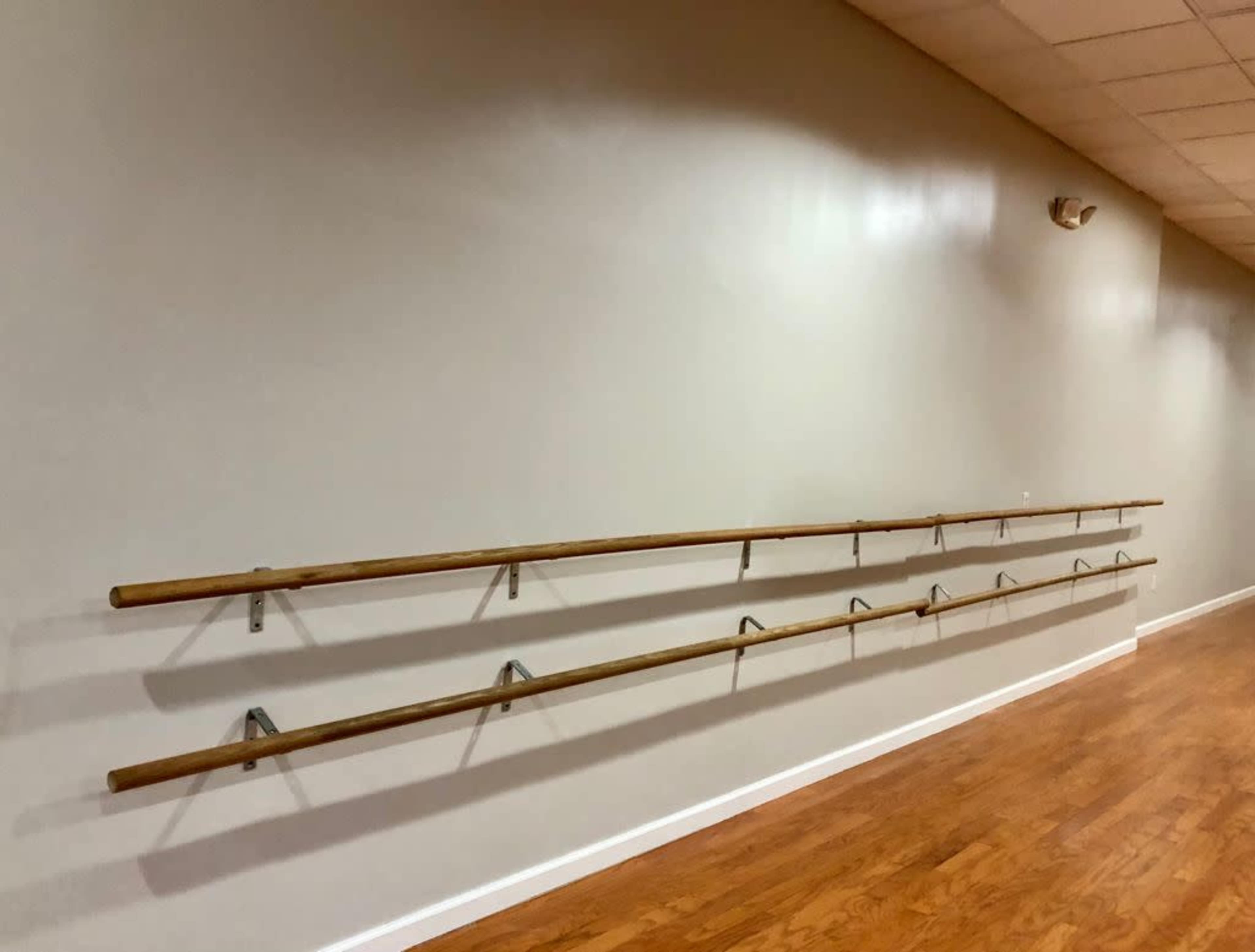 A series of wooden ballet barres mounted on a light-colored wall in a dance studio with a wooden floor.