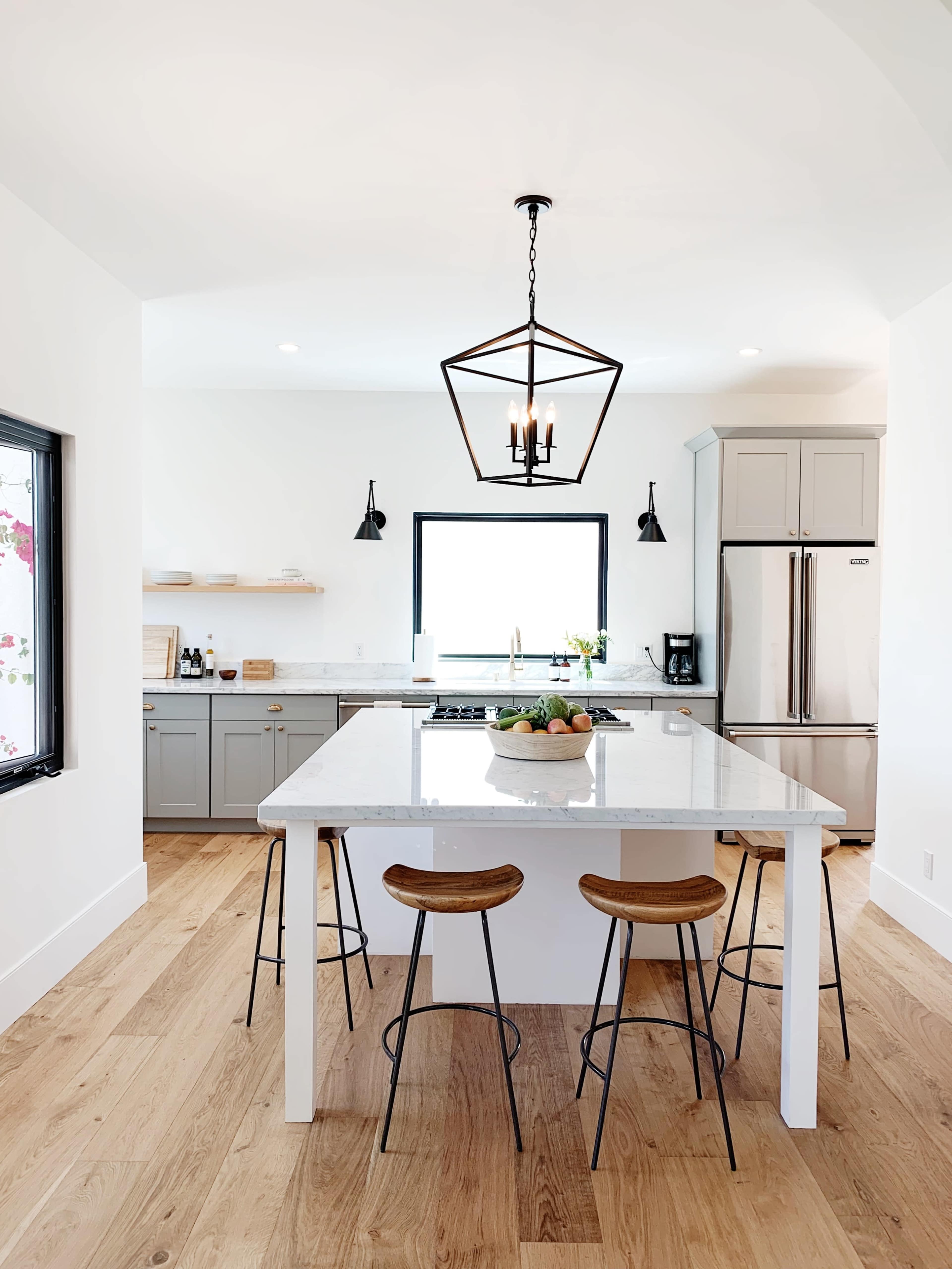 A modern kitchen featuring a central island with three stools, gray cabinetry, and a large window providing natural light.
