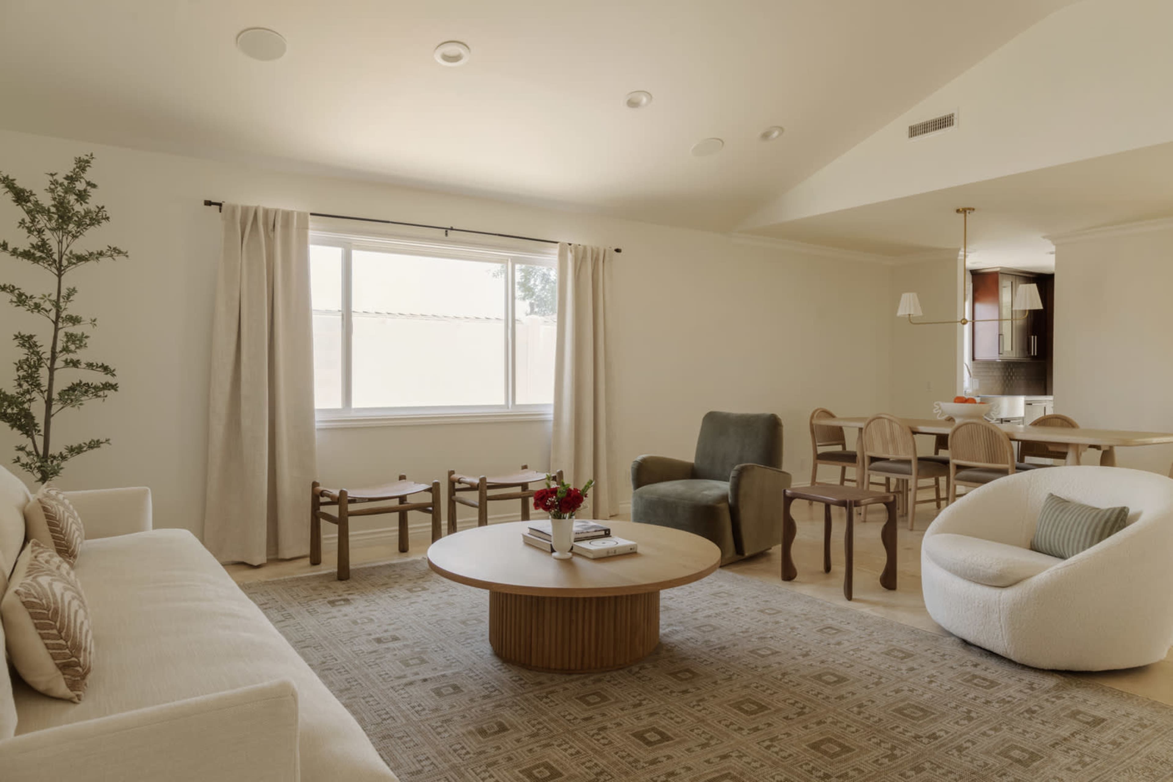 The image features a cozy living room with a light-colored sofa, a round coffee table, a few chairs, and a dining area visible in the background.