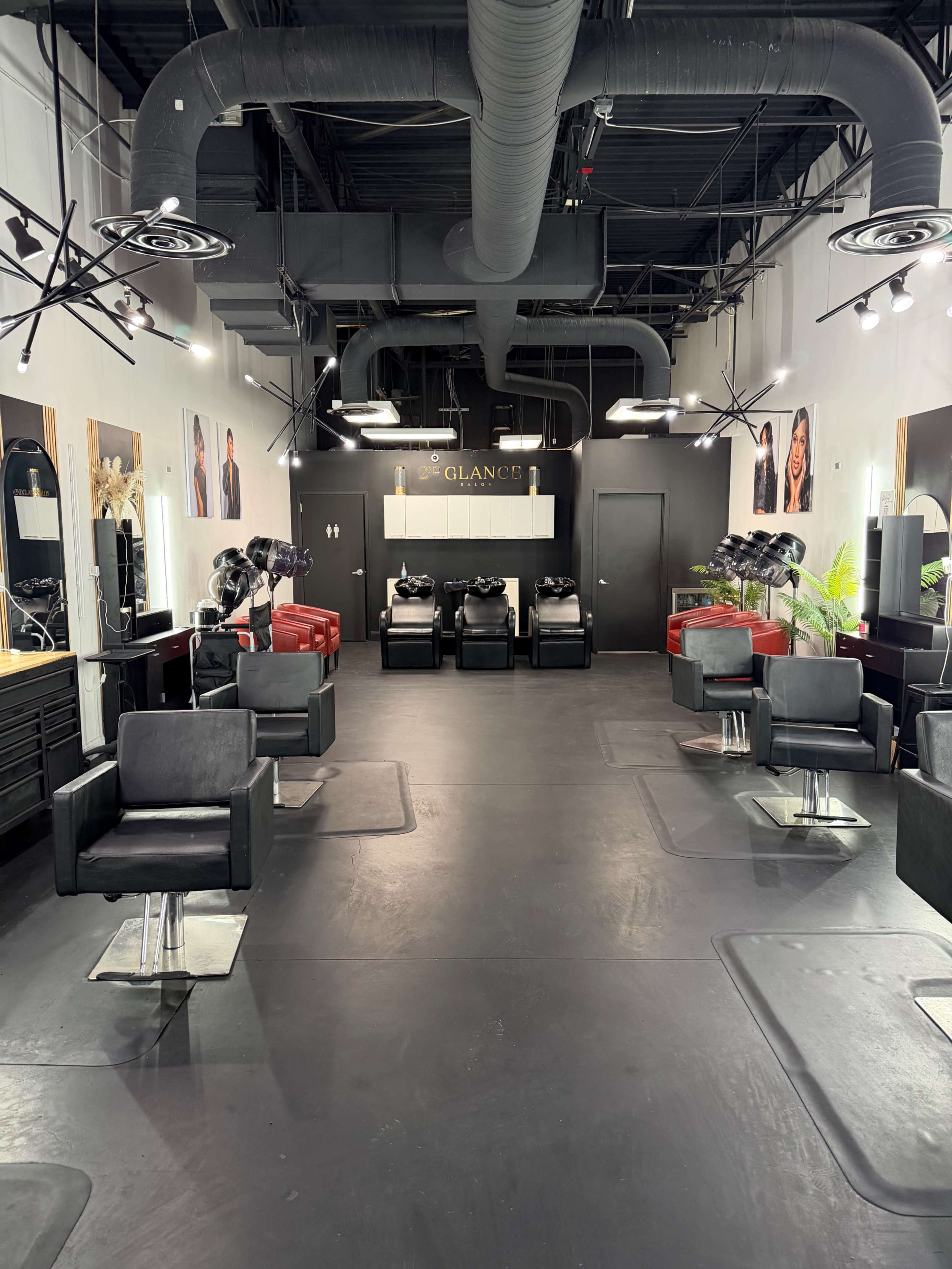 The image shows a modern hair salon with multiple styling stations, black chairs, and bright lighting, featuring mirrors and wall art.