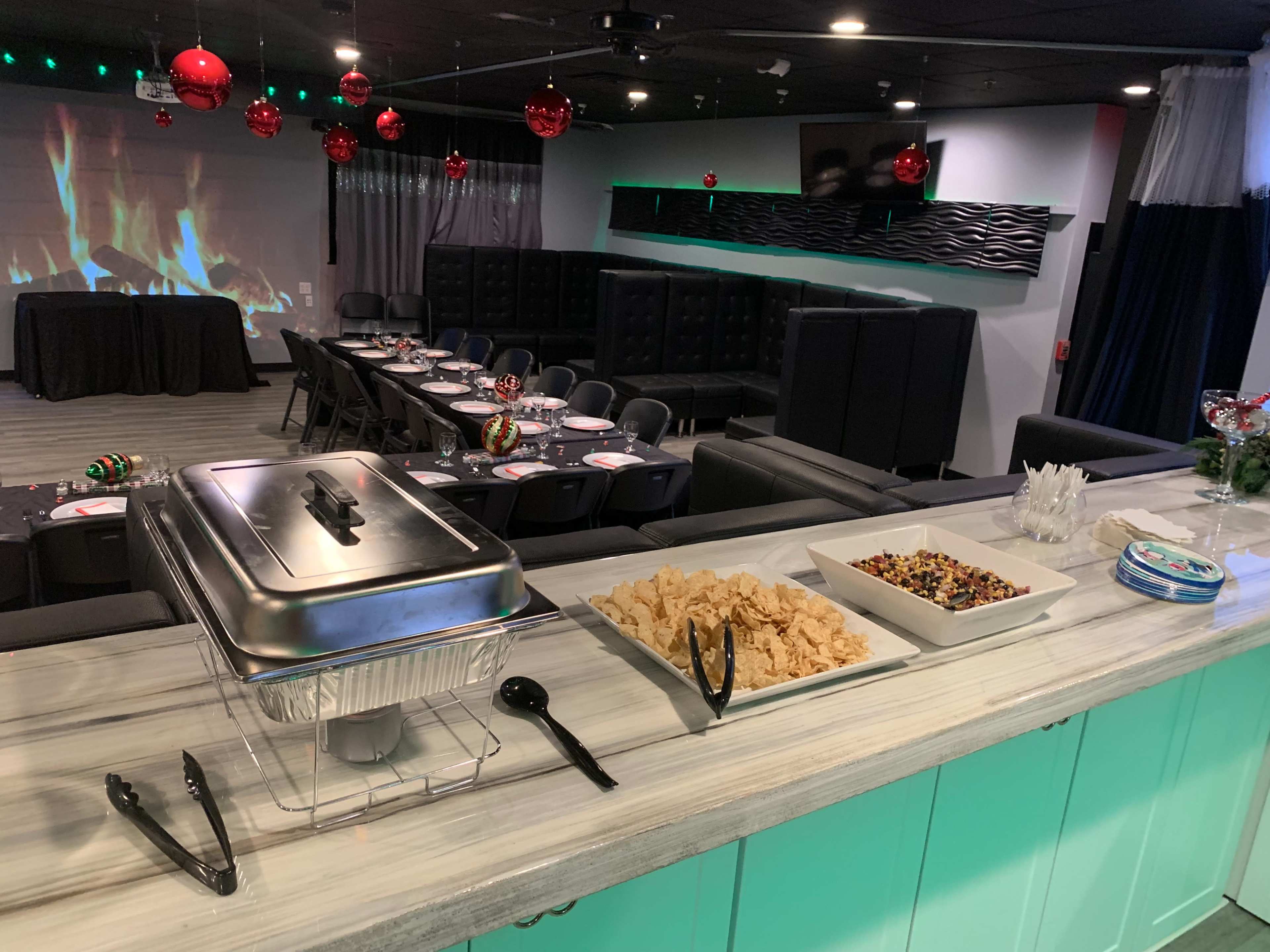 A dining area set up with tables, chairs, and a buffet featuring snacks like chips and candy, decorated with festive red ornaments.