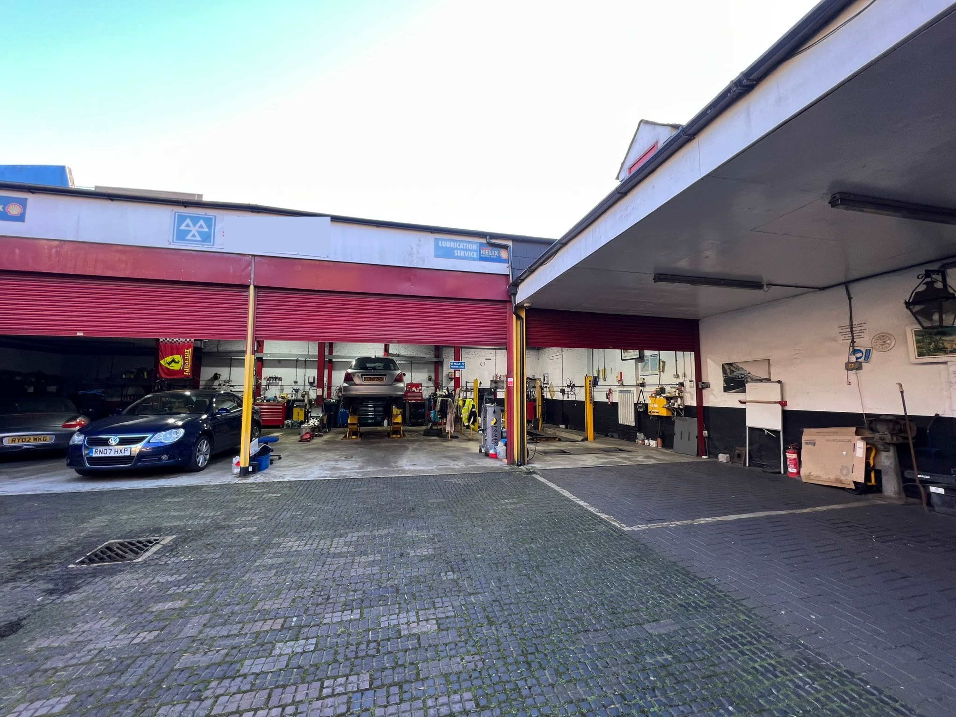 A car service garage divided into two sections, with various cars and mechanics working under overhead lights.