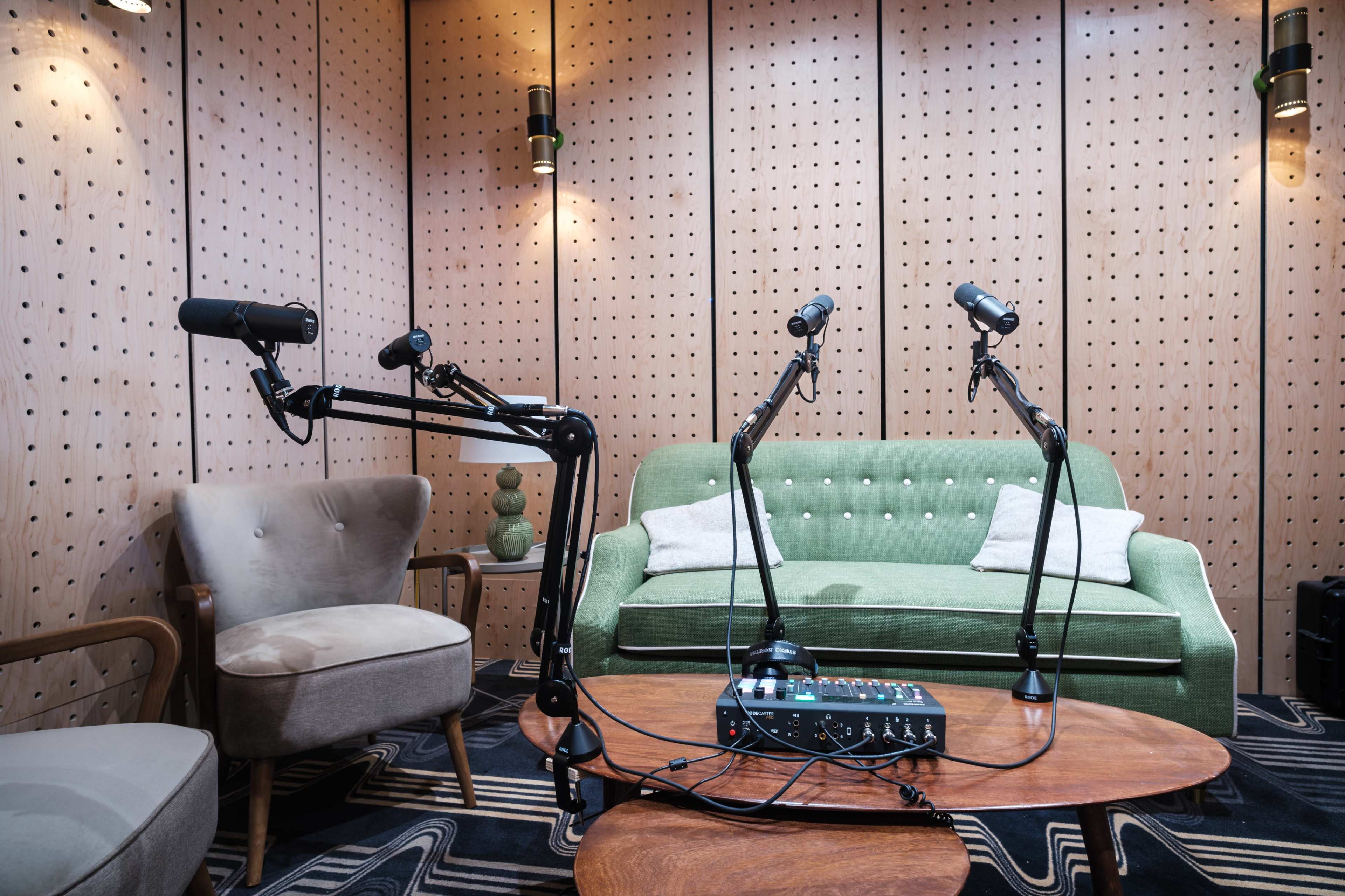 A sound studio with two microphones on adjustable arms positioned near a green sofa and a wooden coffee table.