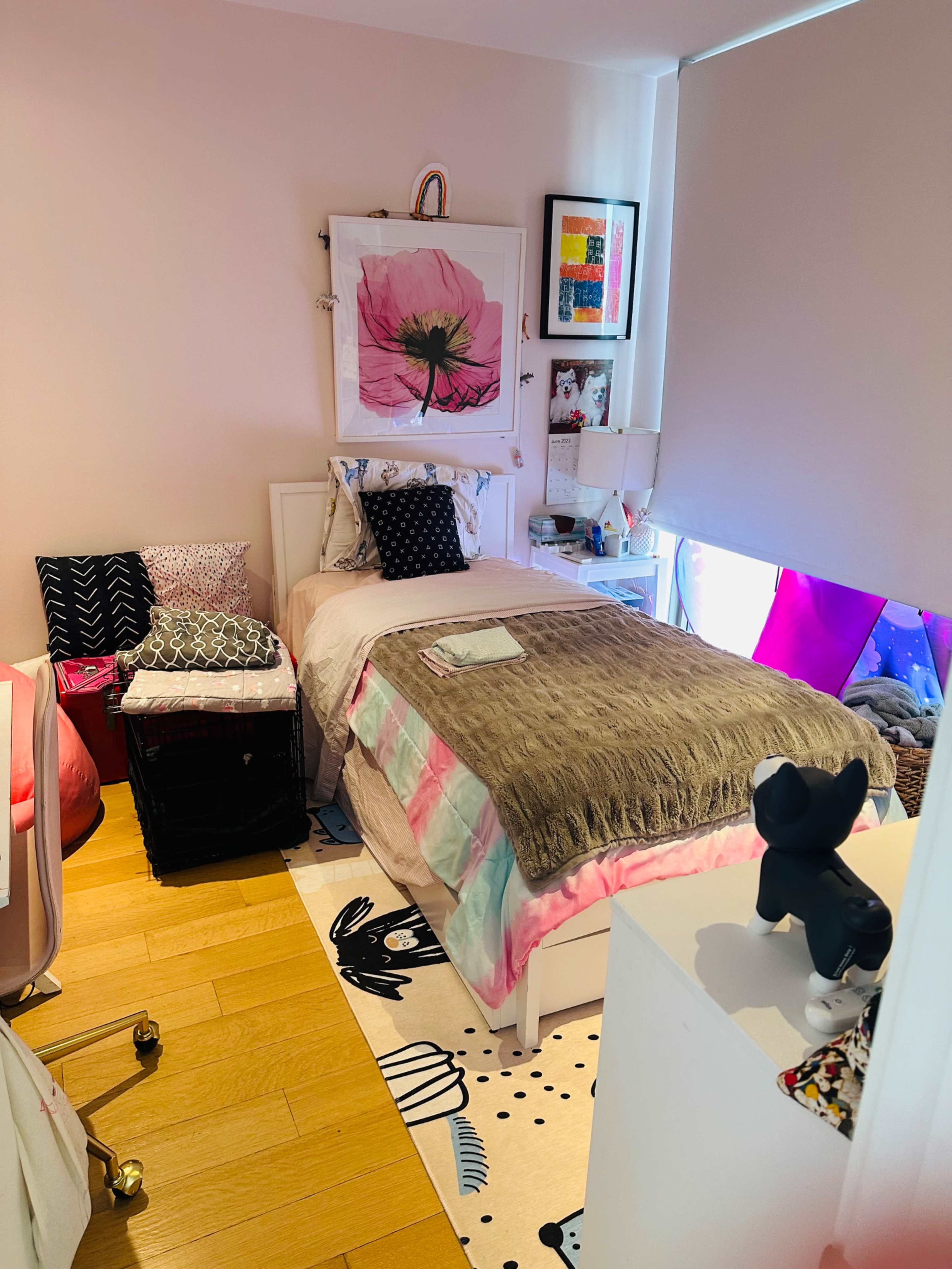 A small bedroom with a single bed, a desk chair, and colorful decor including a floral picture and patterned rugs.