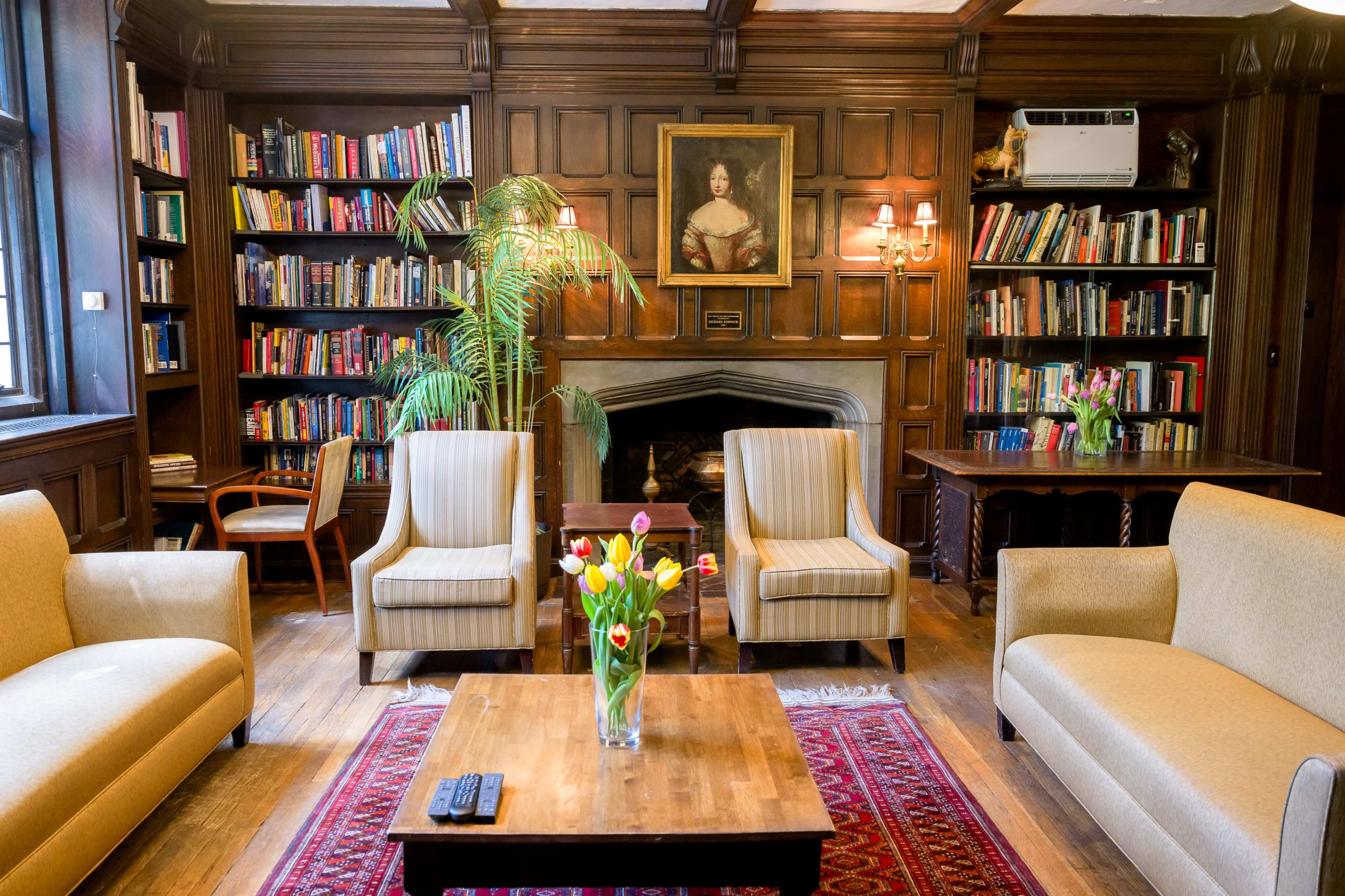 A cozy library with wooden paneling, equipped with bookshelves, comfortable seating, and a decorative flower arrangement on a coffee table.