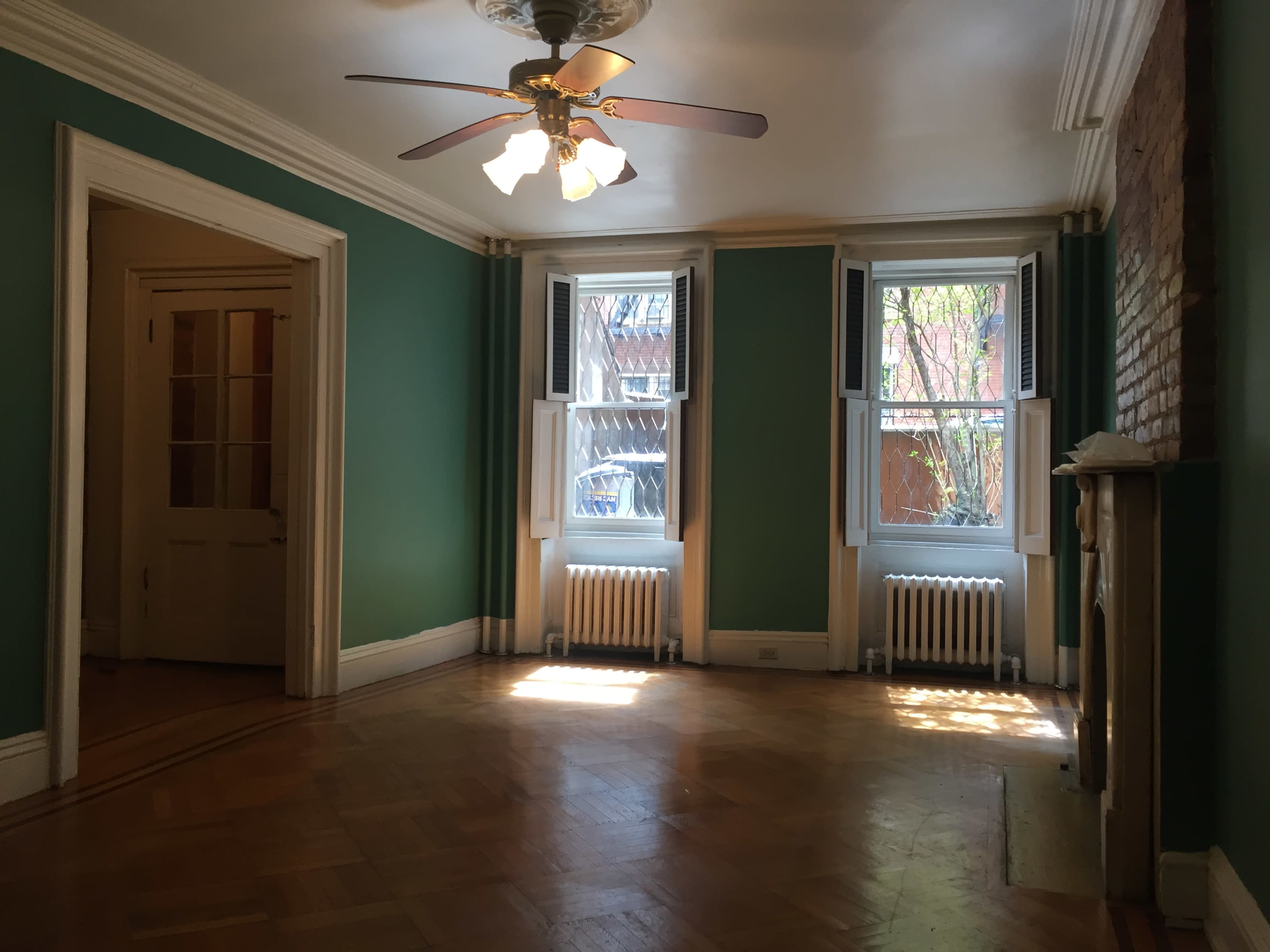 A room with green walls, two windows, a ceiling fan, and a fireplace.
