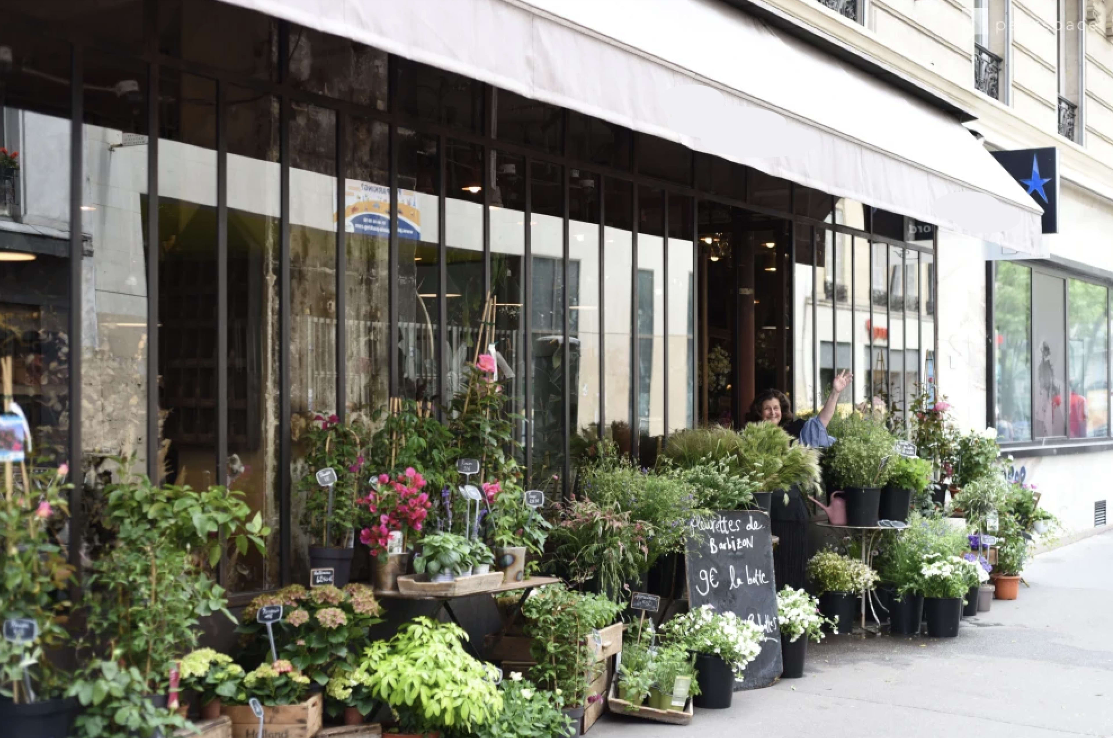 A storefront displays a variety of potted plants and floral arrangements under a canopy.