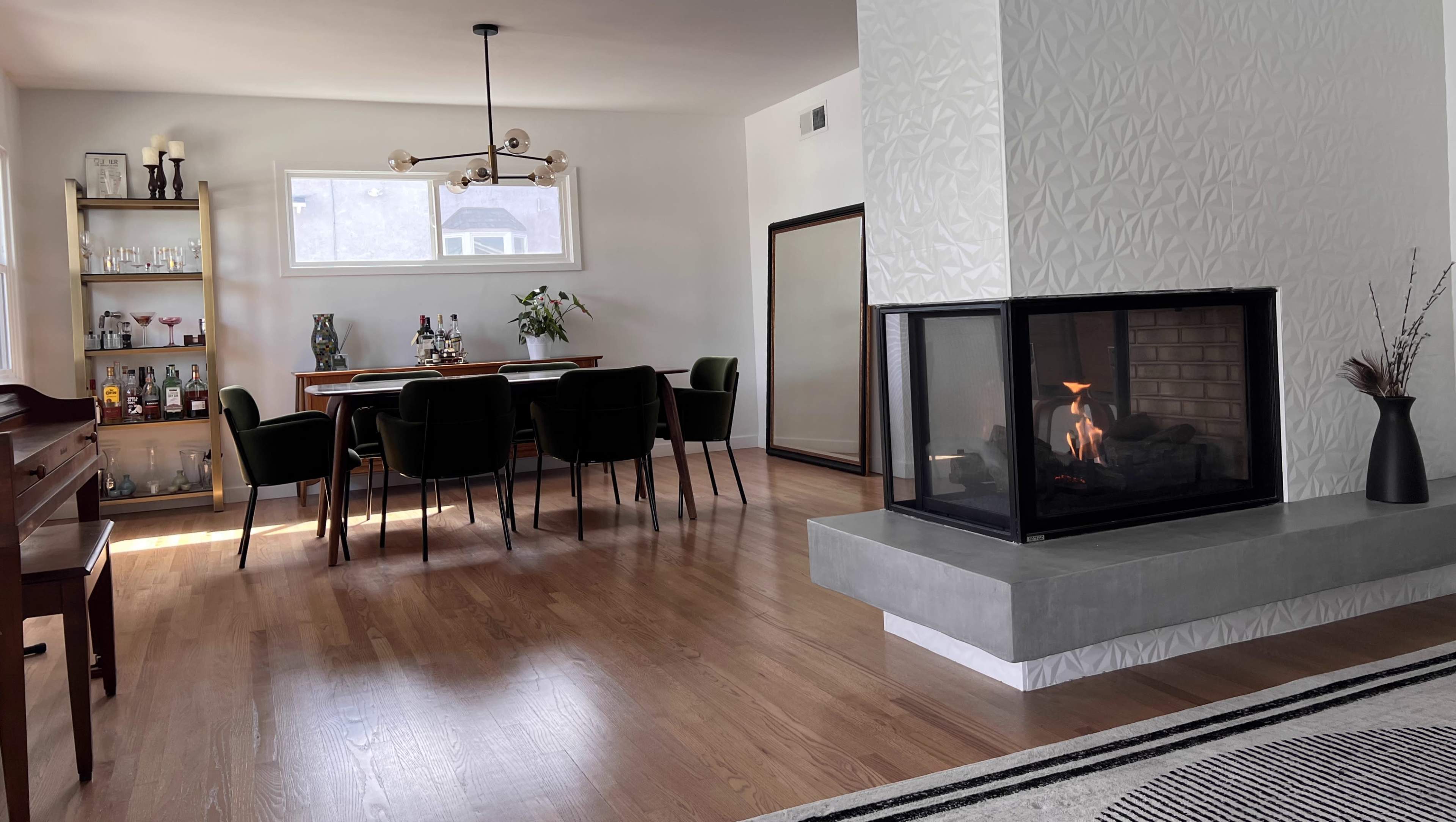 A modern living space features a dining area with a wooden table and dark chairs, alongside a fireplace with a sleek design.