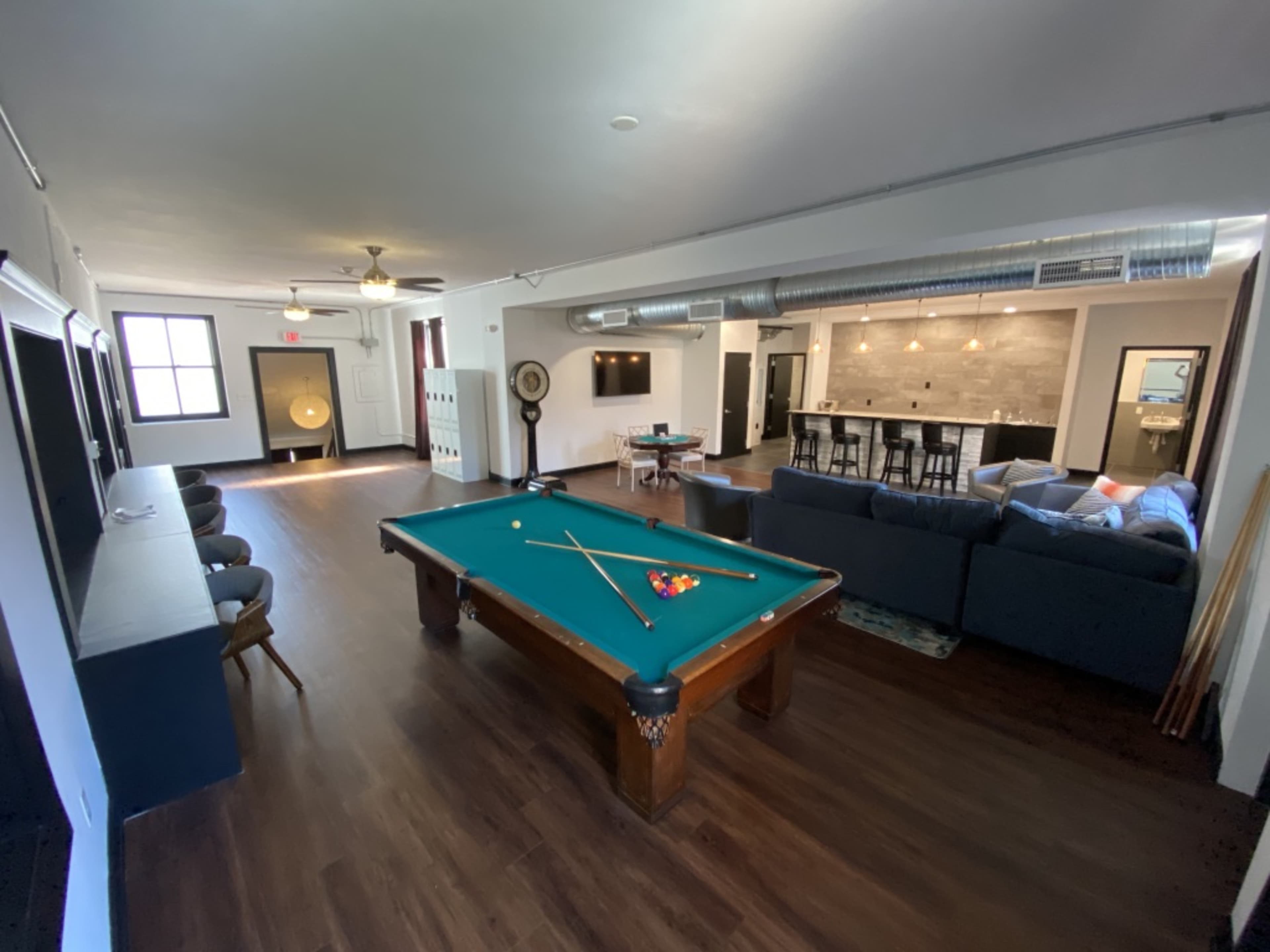 The room features a pool table in the foreground, with a seating area and a bar in the background.