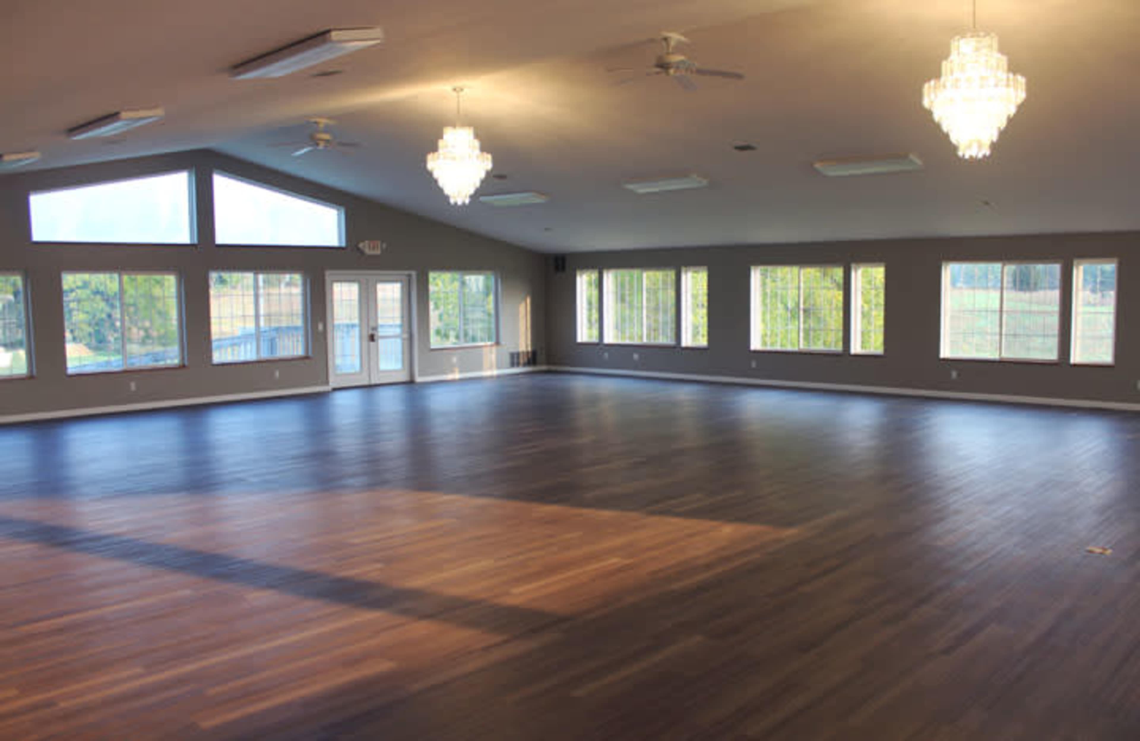 A spacious room with large windows, wooden floors, and two crystal chandeliers.