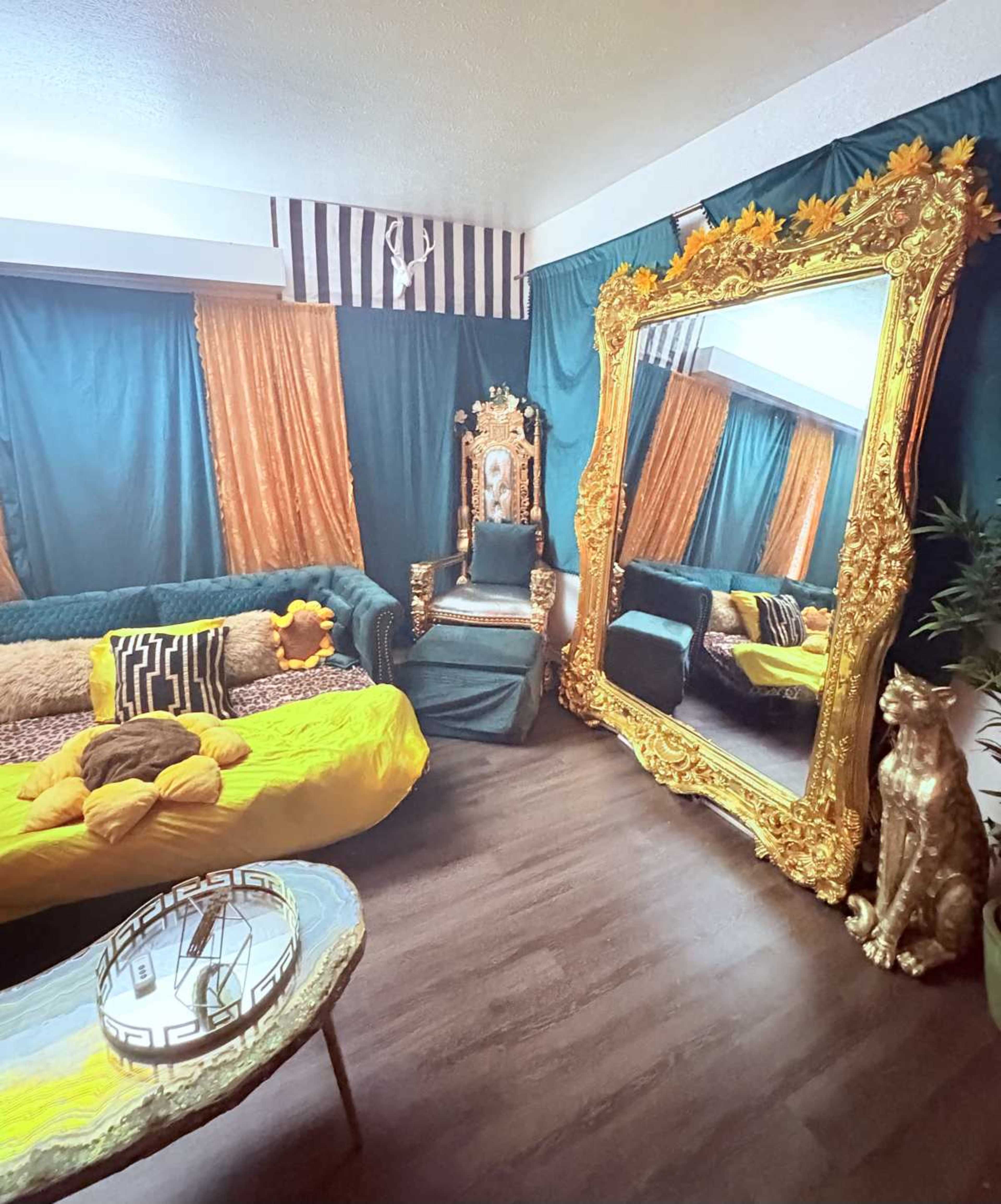 The room features opulent decor with a large ornate mirror, a throne-like chair, vibrant fabrics, and a combination of modern and classical furniture elements.