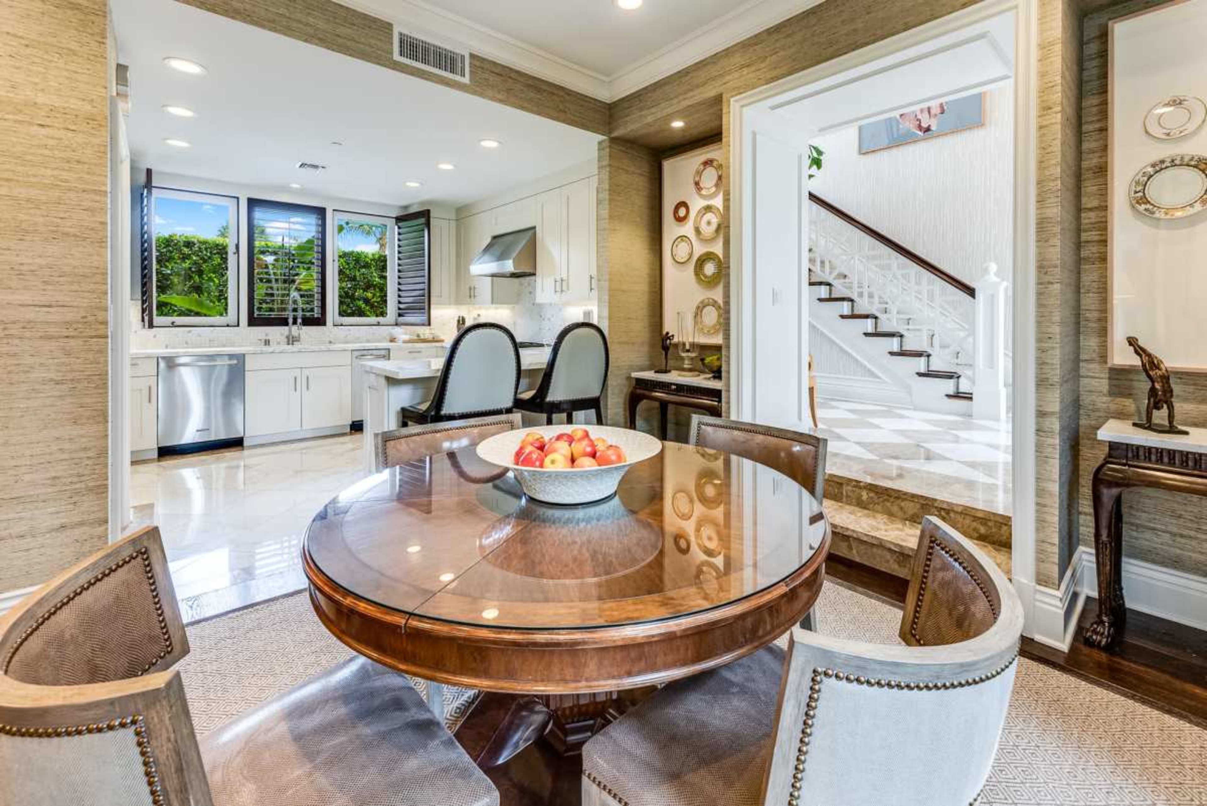 The image depicts a modern kitchen area with a round wooden table set for dining, adorned with a bowl of apples, and a staircase visible in the background.