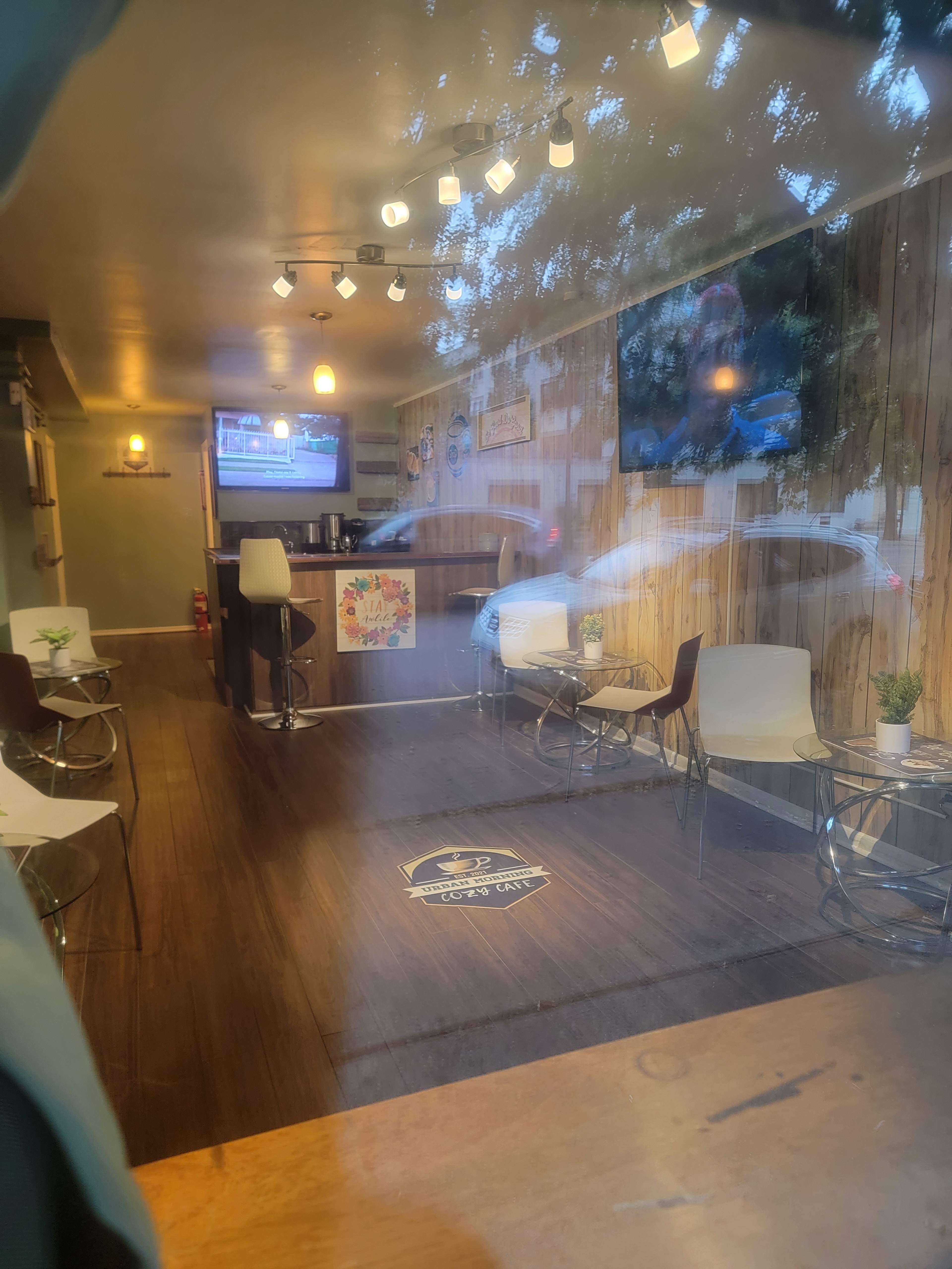 The image shows a cozy café interior with wooden paneling, modern seating, and a television mounted on the wall.