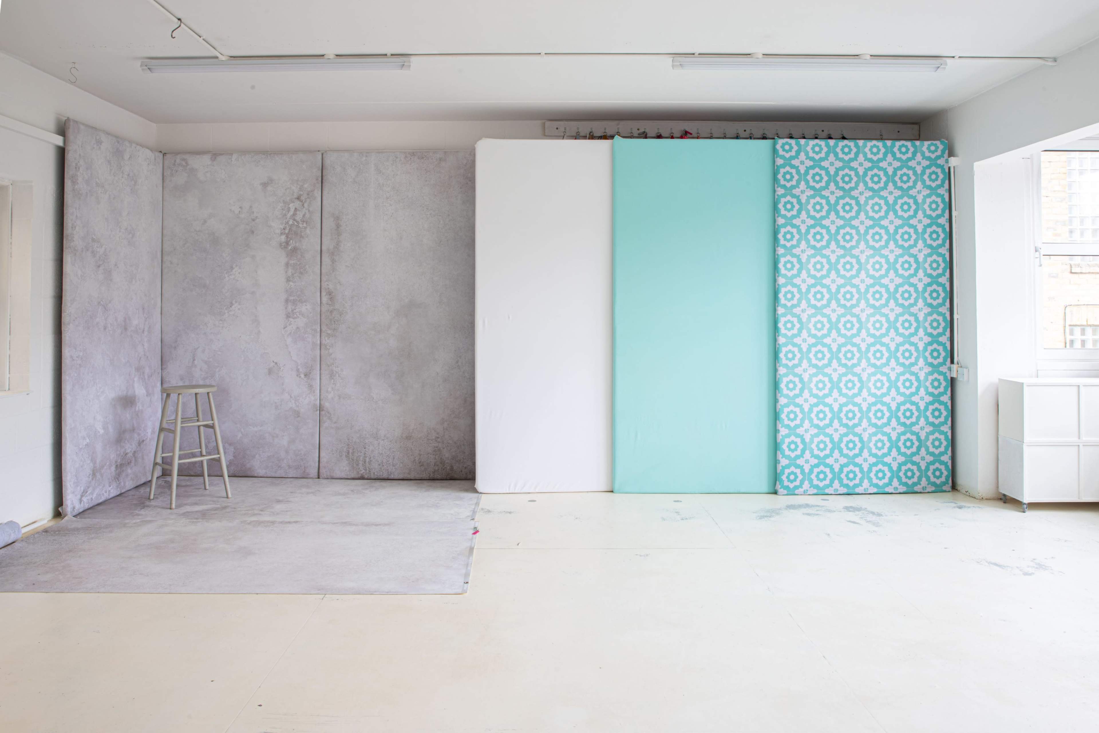 A photography studio with multiple backdrops including a gray, white, light blue, and patterned panel arranged against a white wall.