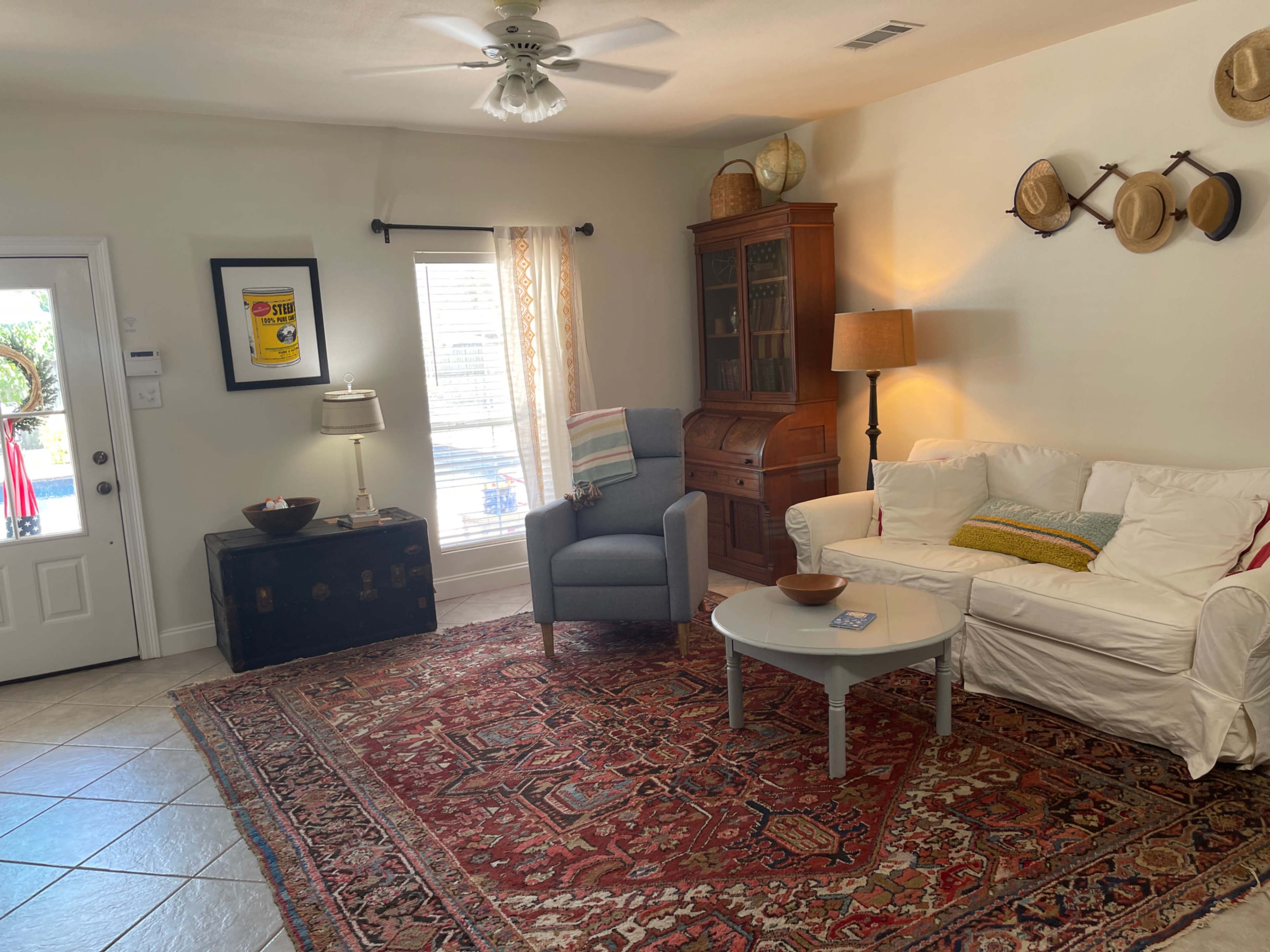 The image shows a cozy living room with a white sofa, an armchair, a coffee table, and various decorative items on the walls and furniture.