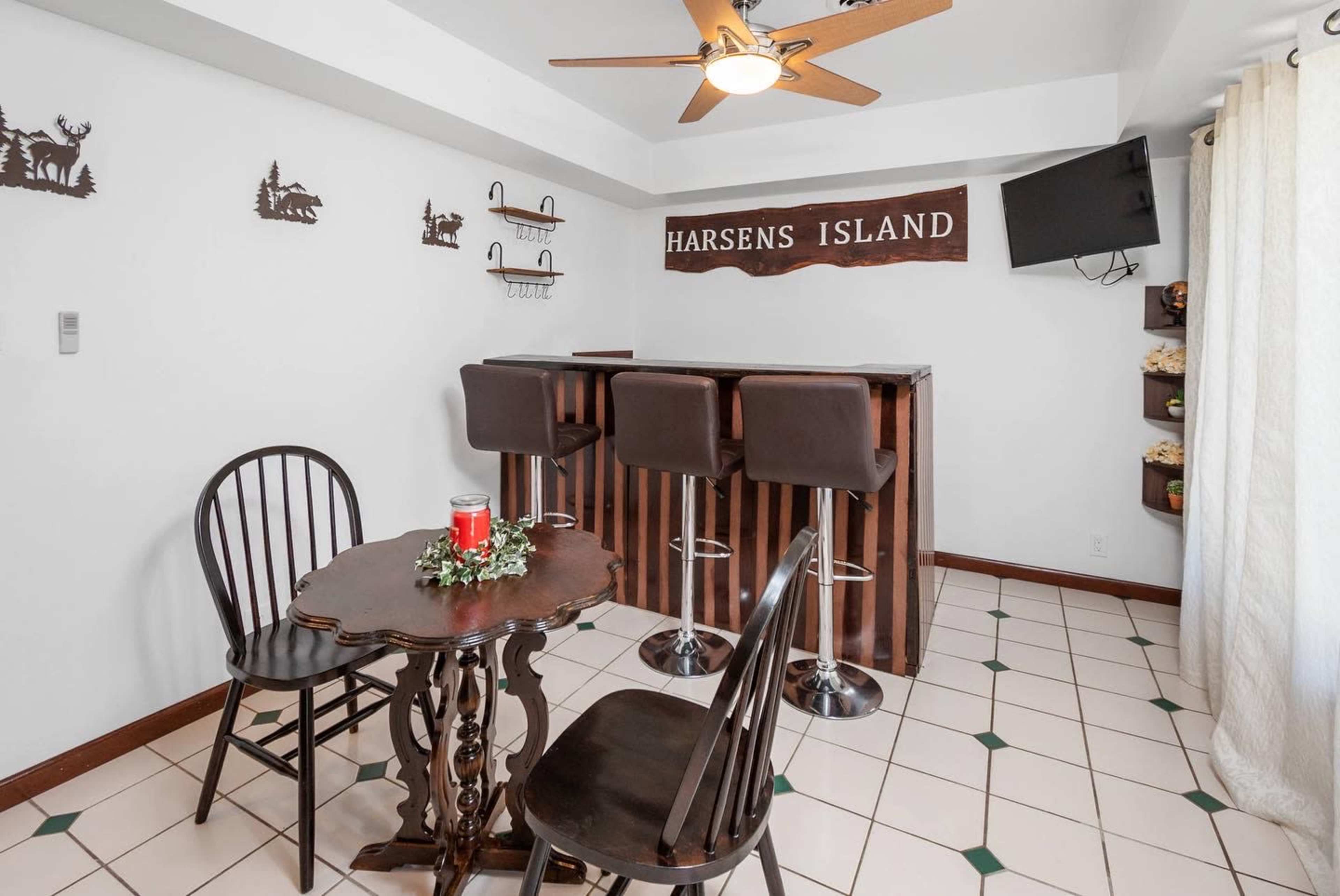 A small bar area with a wooden countertop, two stools, a table with two chairs, and a wall-mounted television.