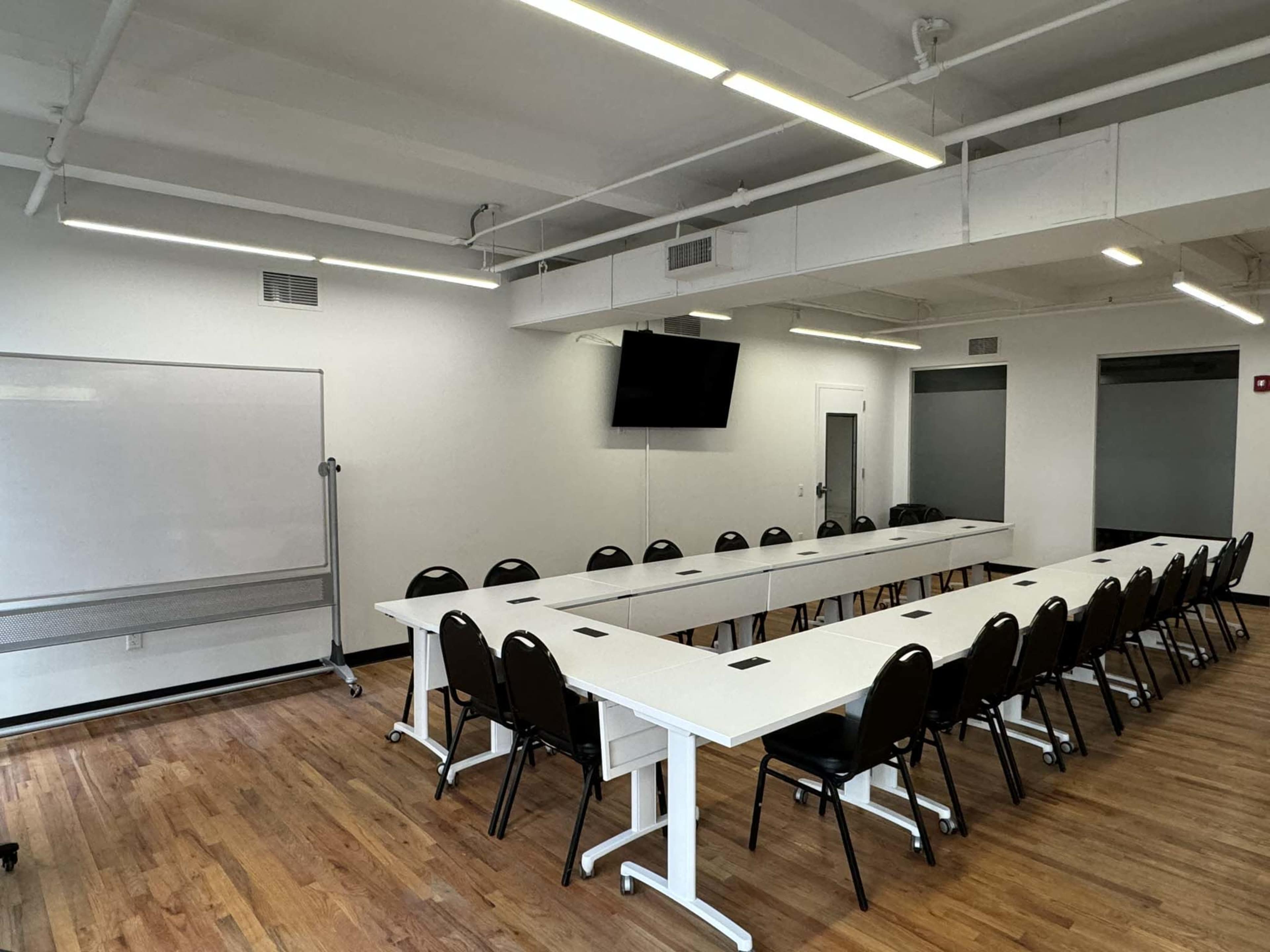 A large conference room features a long white table with black chairs, a television mounted on the wall, and a whiteboard.