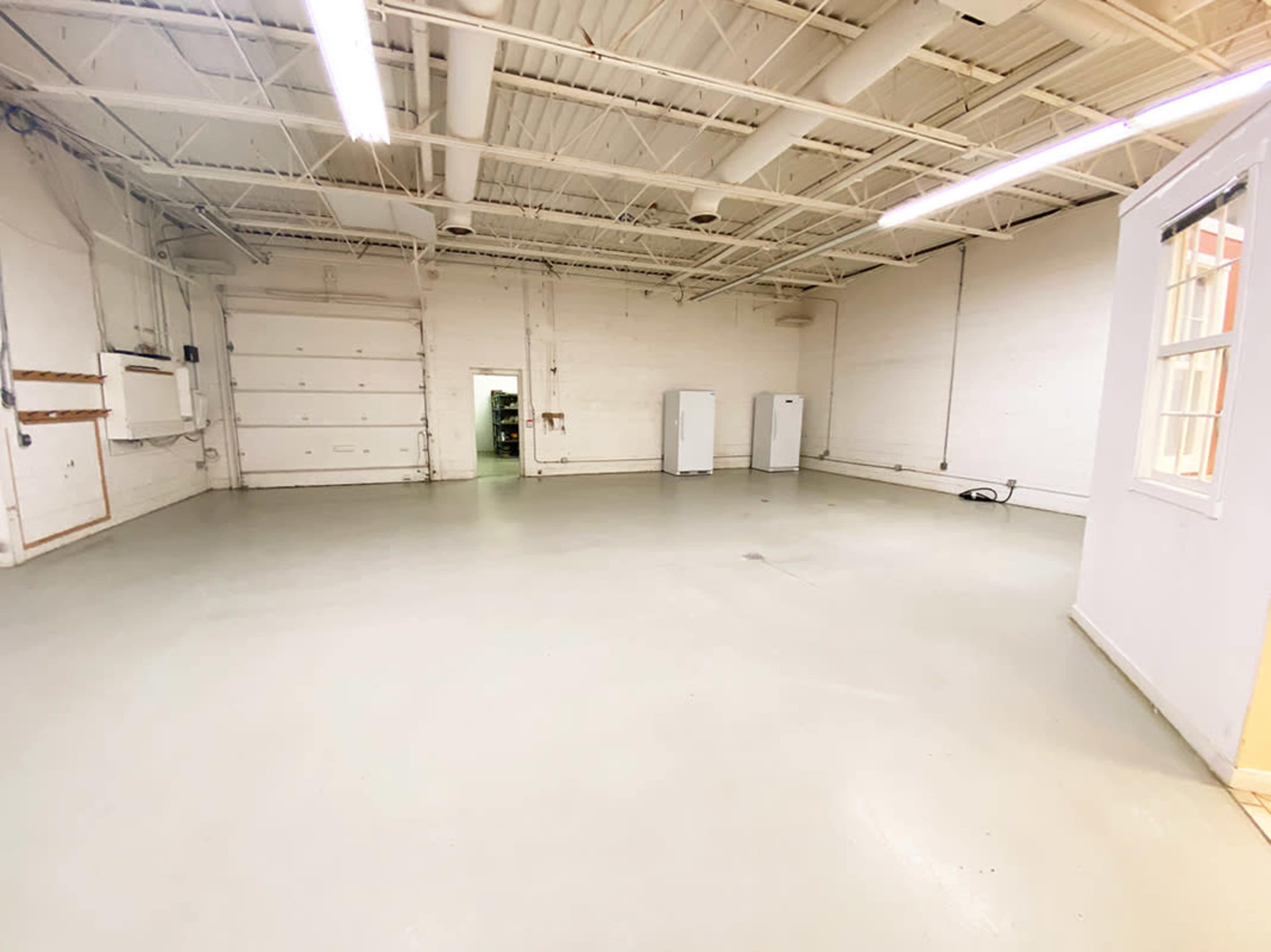 An empty industrial space with a concrete floor, white walls, and several appliances against the walls.
