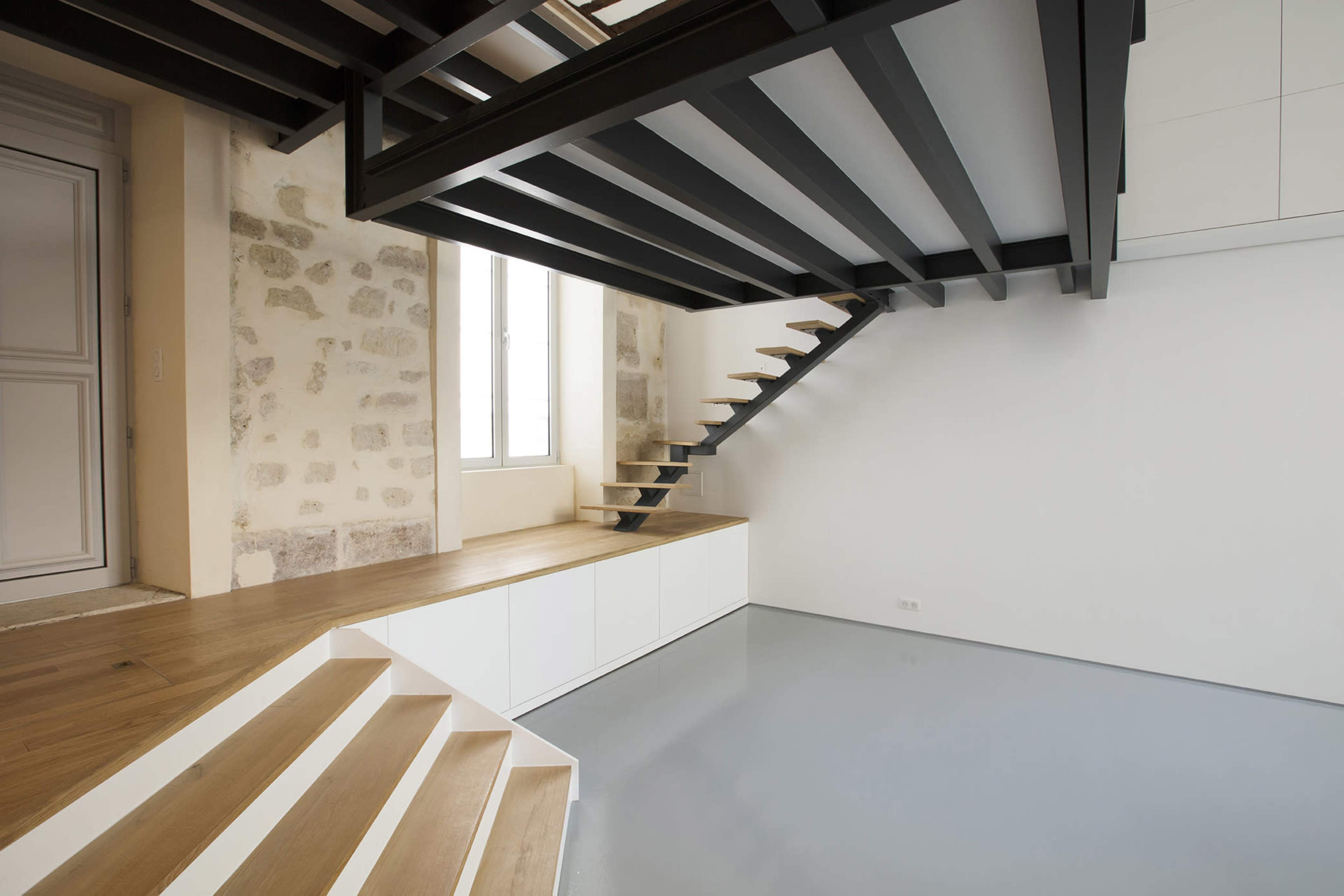 The image shows a modern interior space featuring a staircase with wooden steps, a black metal railing, and a combination of stone and white walls.