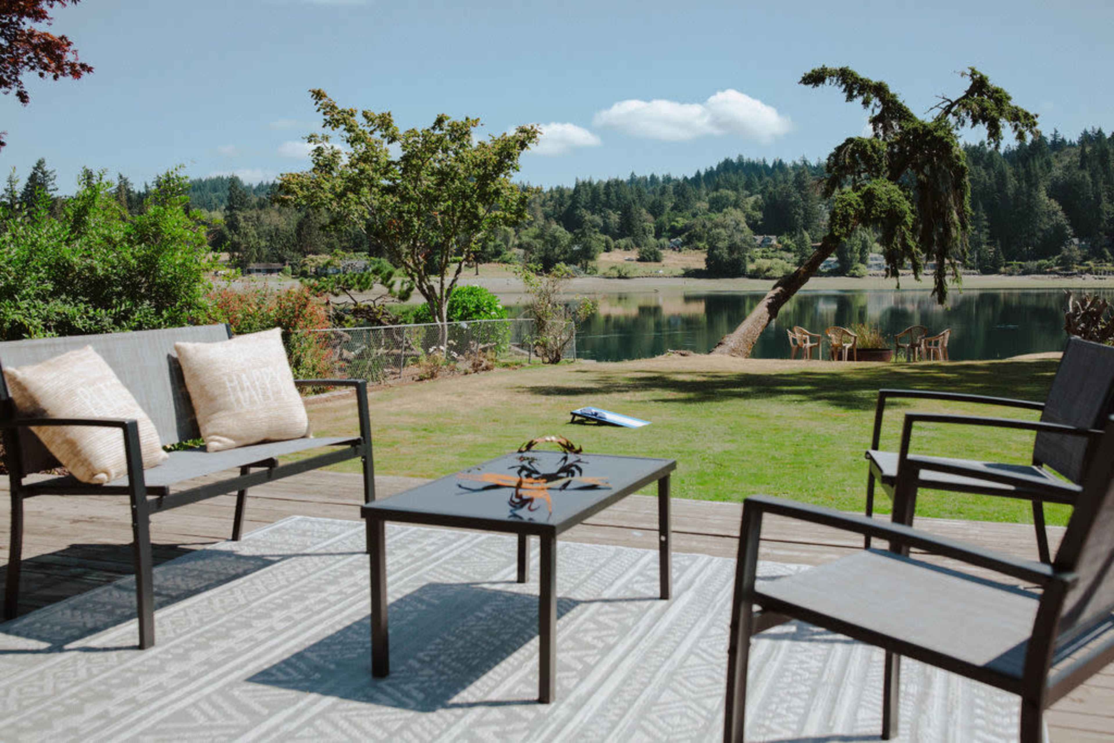 A patio featuring four chairs and a coffee table overlooks a serene lake and green landscape.