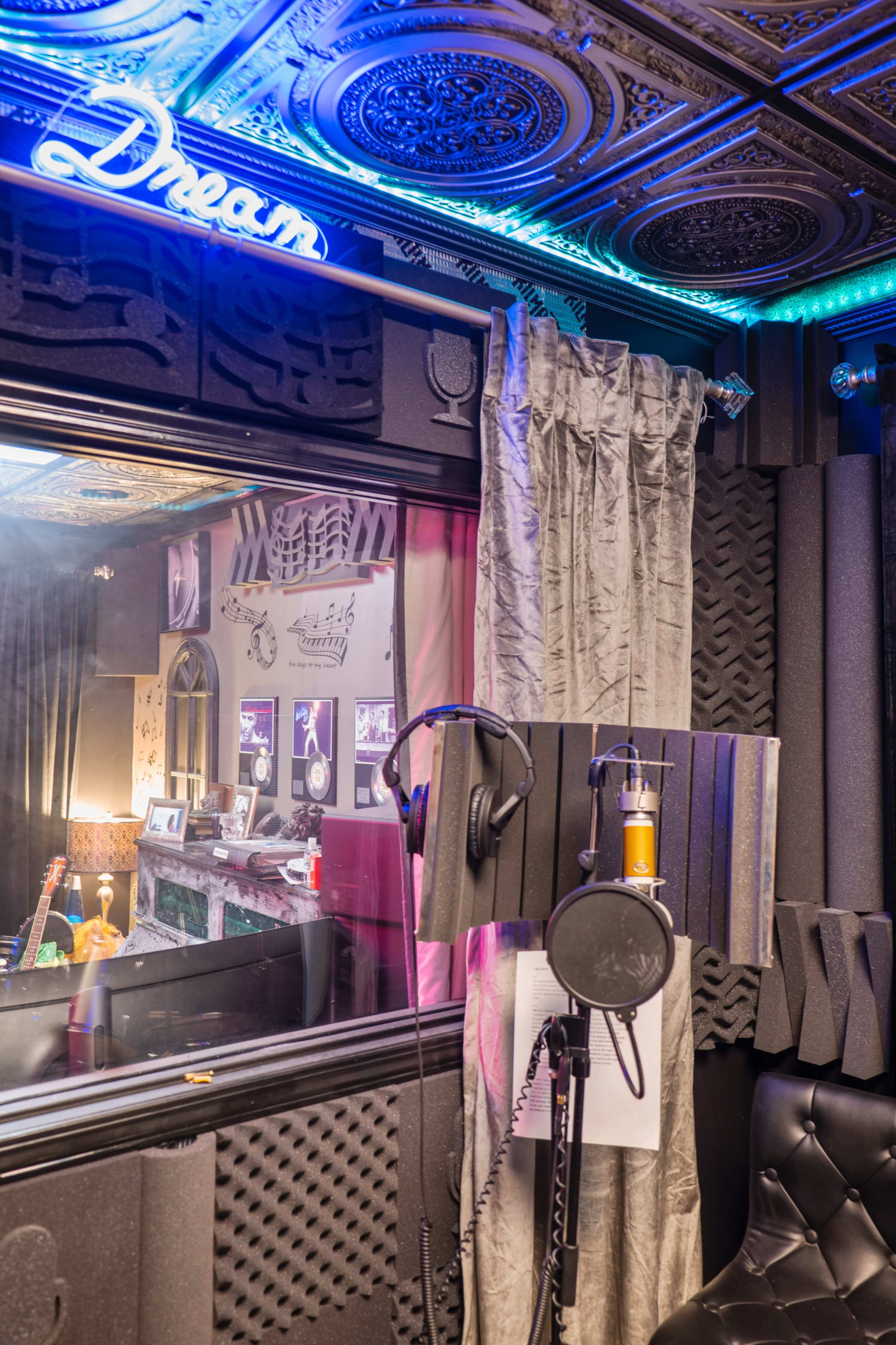 A recording studio is shown with soundproofing panels, a microphone set up, and a framed sign that reads "Dream" illuminated above.