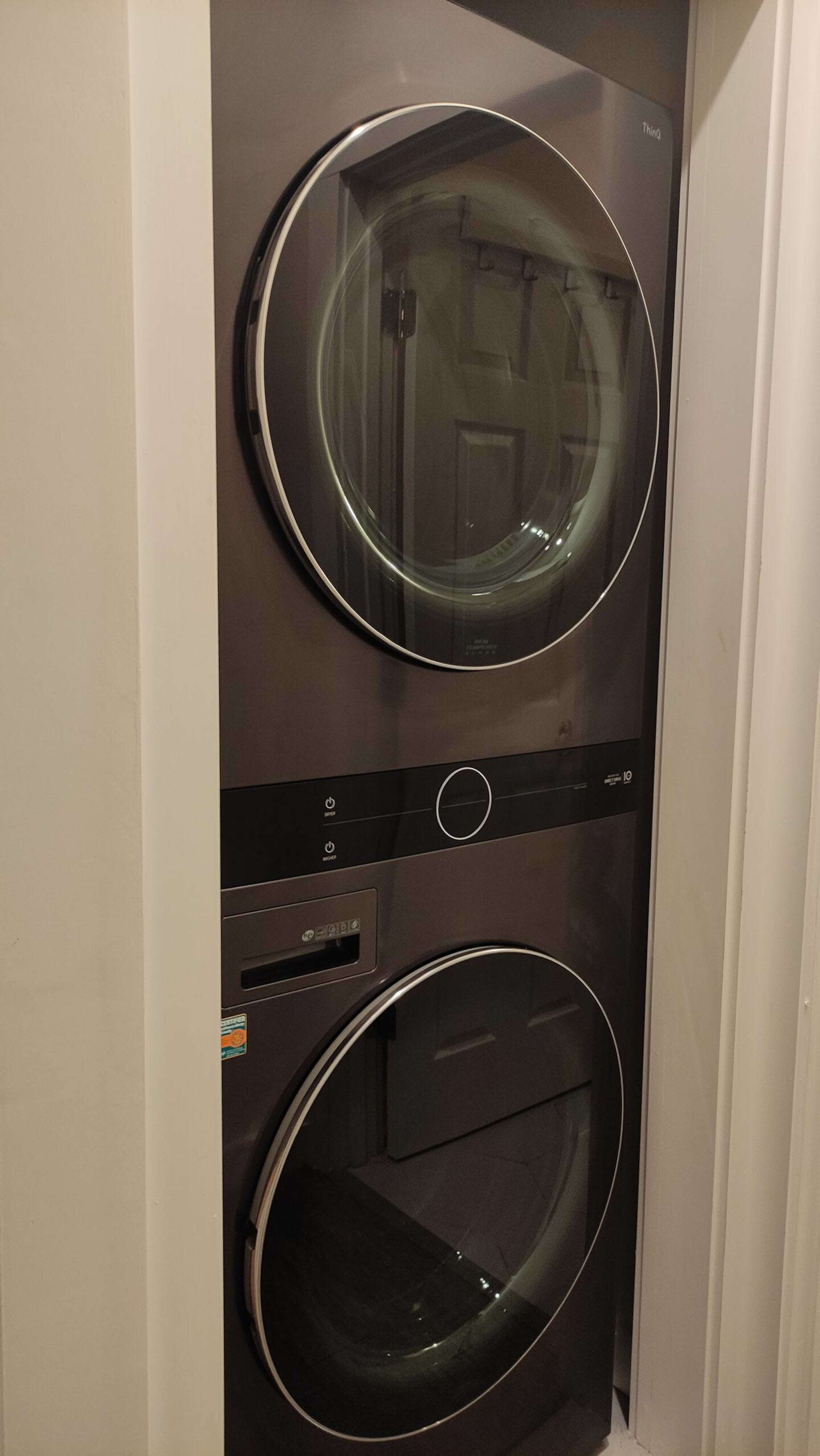 The image shows a stacked washer and dryer unit in a narrow space with a dark finish and circular doors.