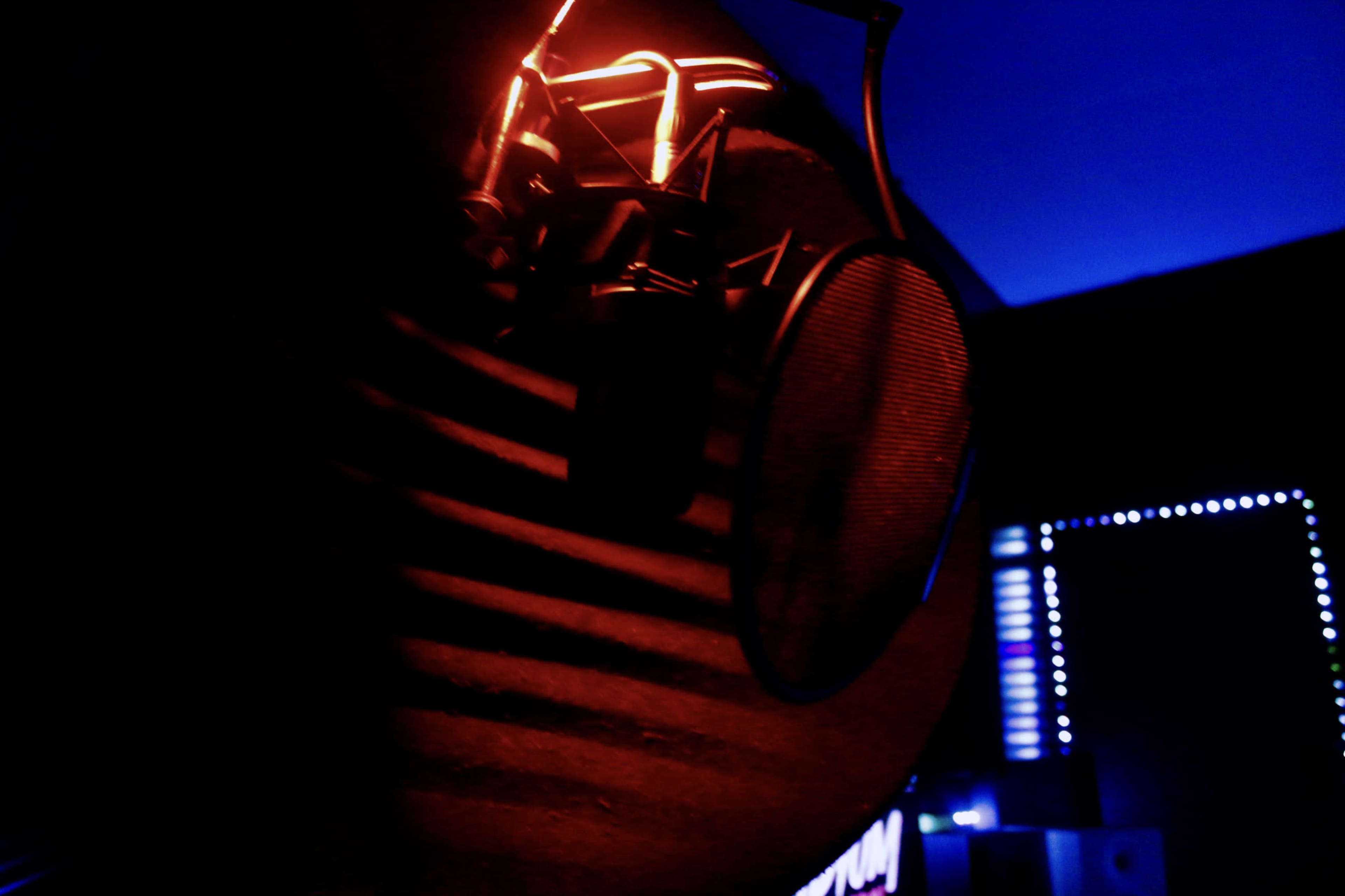 A microphone is illuminated by red and blue lights in a dimly lit recording studio.