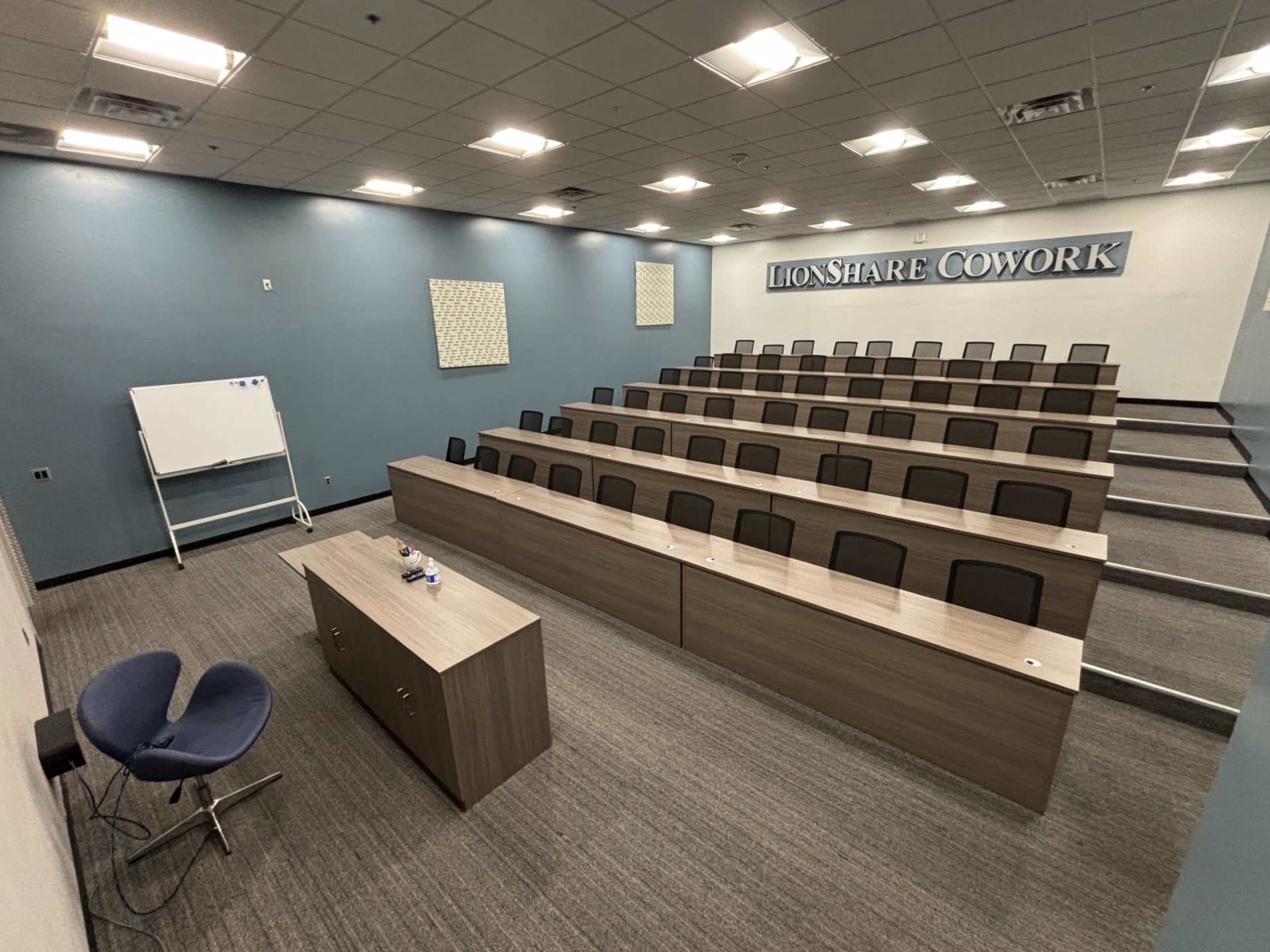 A modern classroom set up with tiered seating, a whiteboard, and a presentation area in a co-working space.